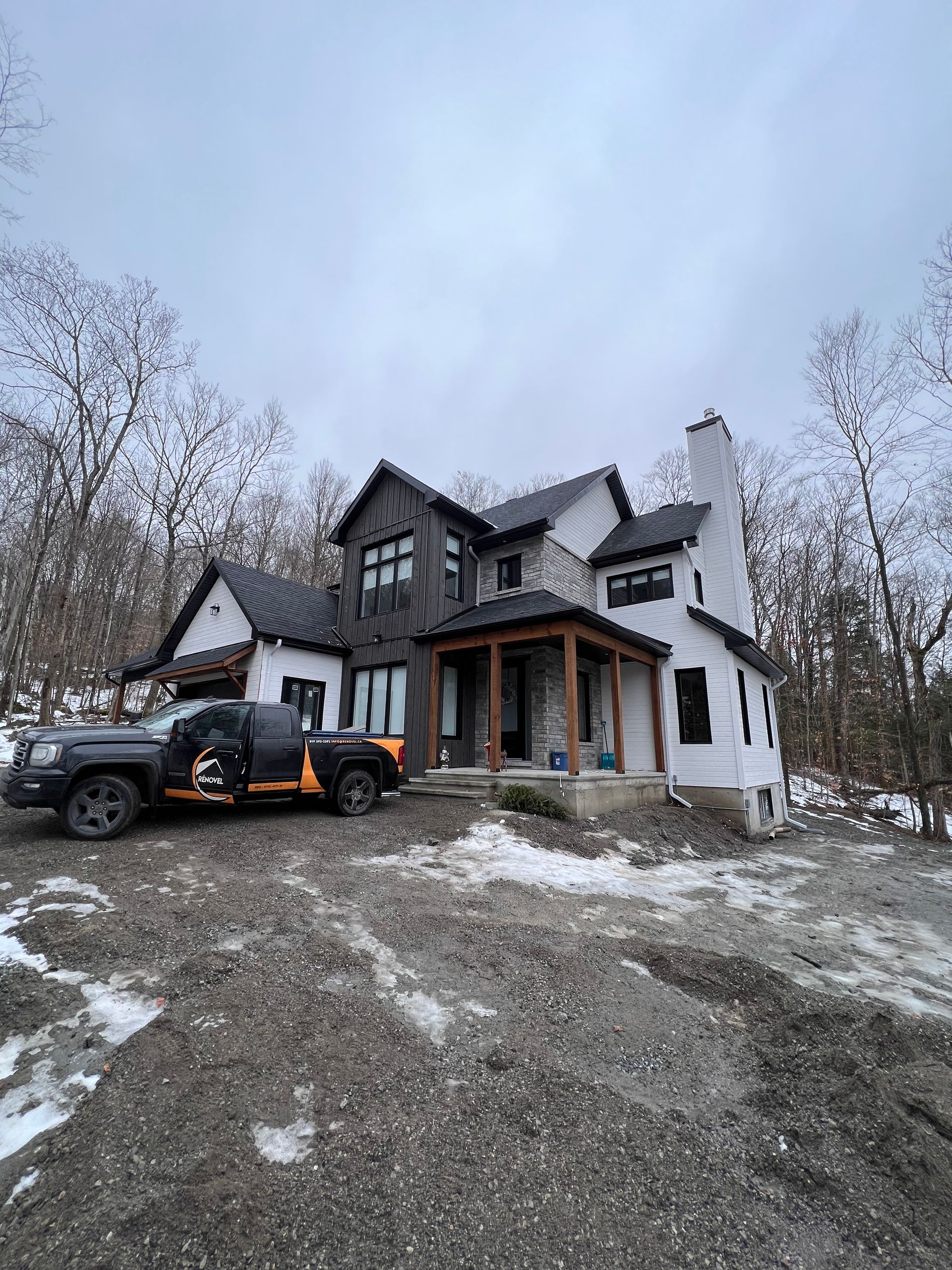 Allée enneigée avec deux camions garés à côté d'une grande maison blanche et d'arbres dénudés