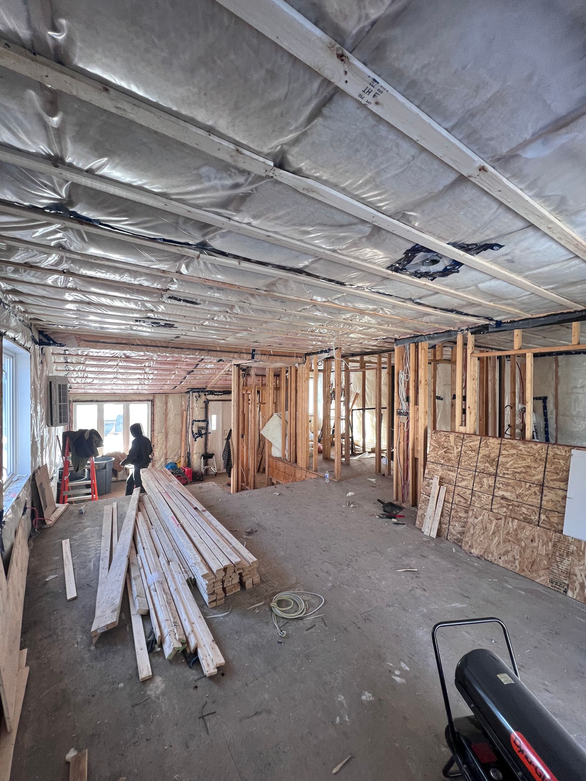 Intérieur en travaux avec charpente apparente, isolation et ouvriers dans une pièce partiellement terminée.