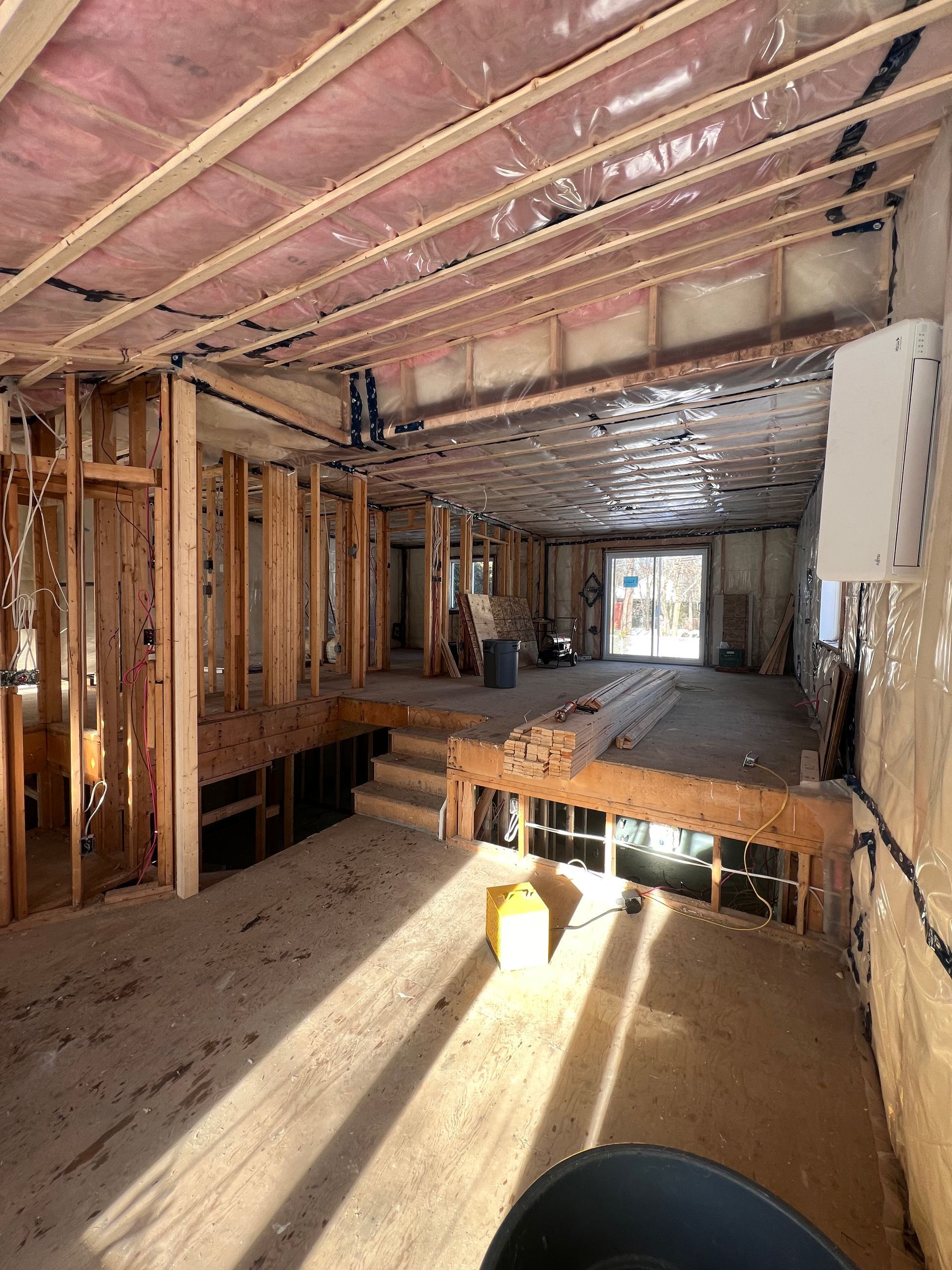 Intérieur d'une maison en construction, avec charpente en bois apparente, isolation et lumière du soleil qui entre en rayon.