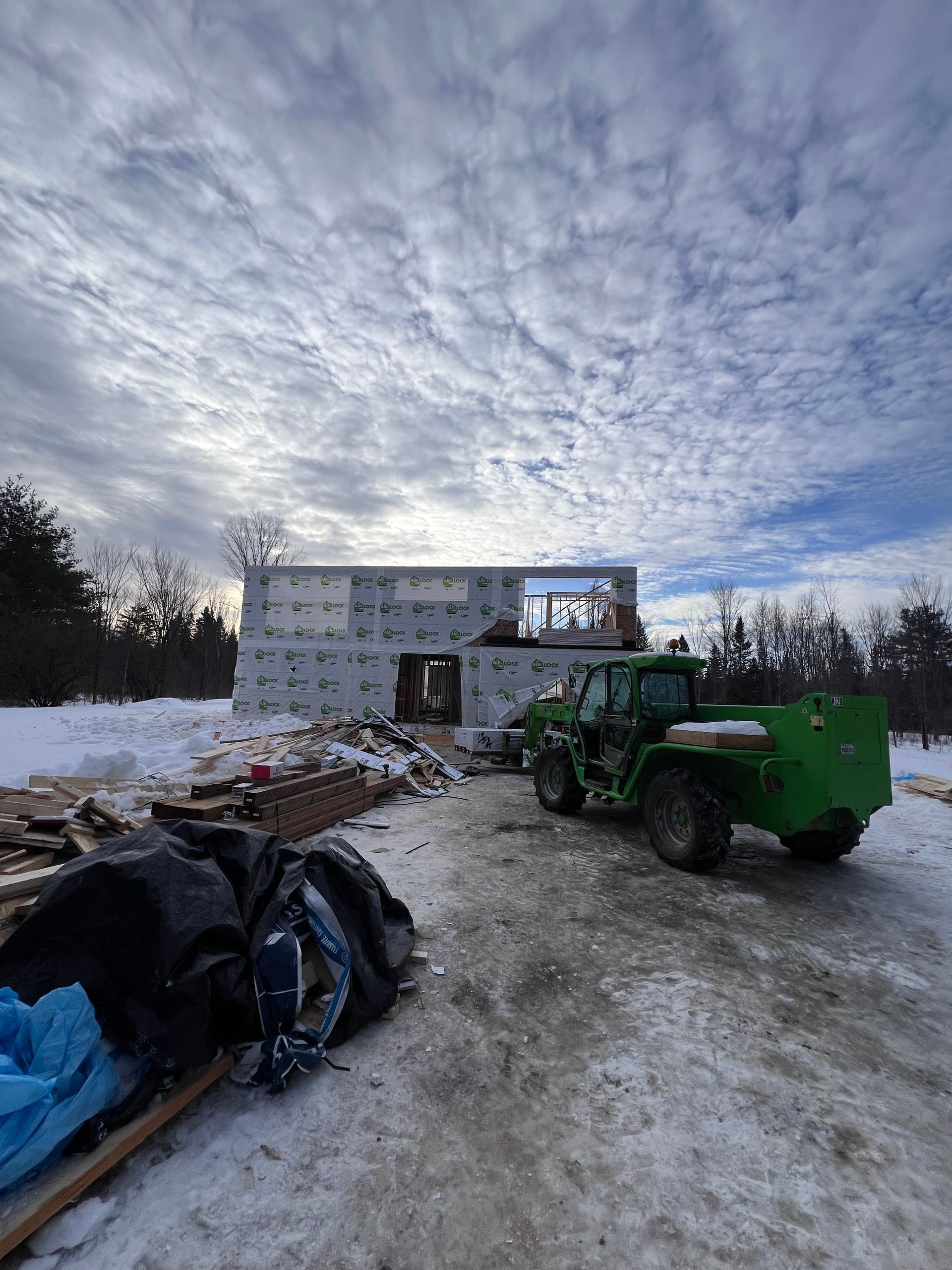 Chantier de construction avec une chargeuse verte sur un sol enneigé à côté d'un bâtiment en béton partiellement construit sous un ciel nuageux