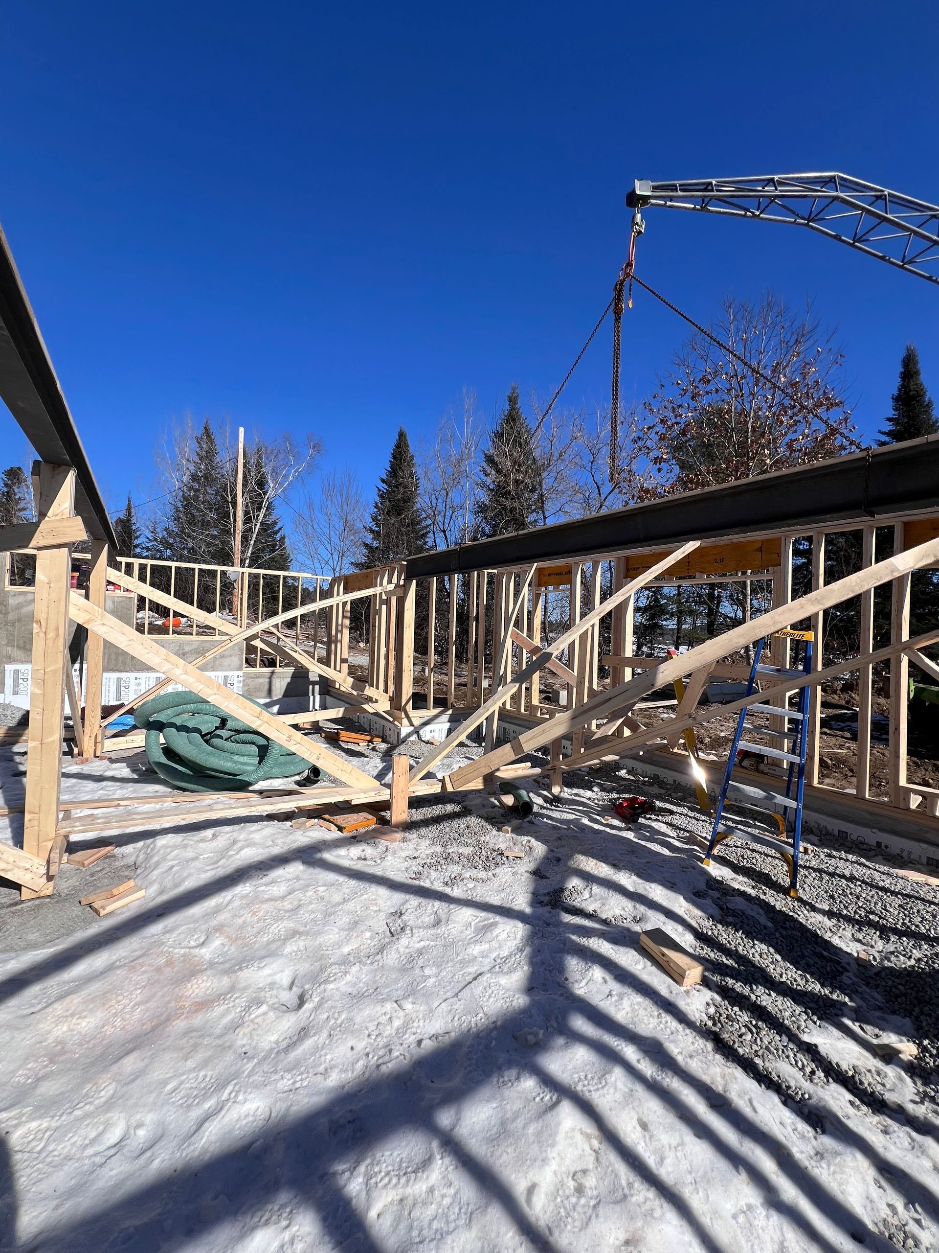 Charpente en bois d'une maison en construction sur un terrain enneigé sous un ciel bleu azur