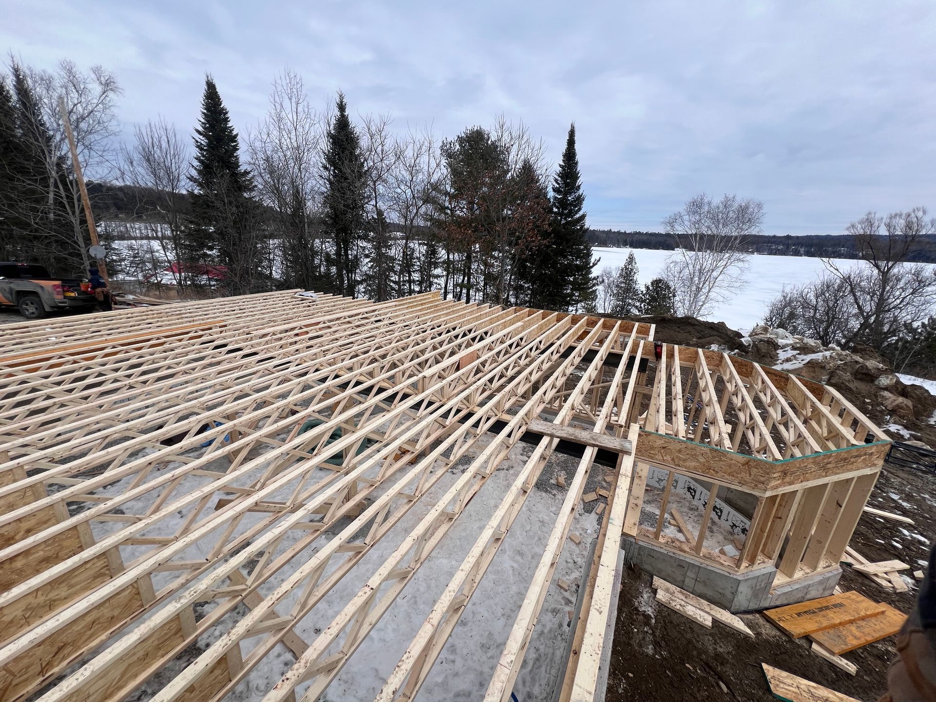 Charpente de toit en bois en construction sur un versant enneigé avec des arbres en arrière-plan