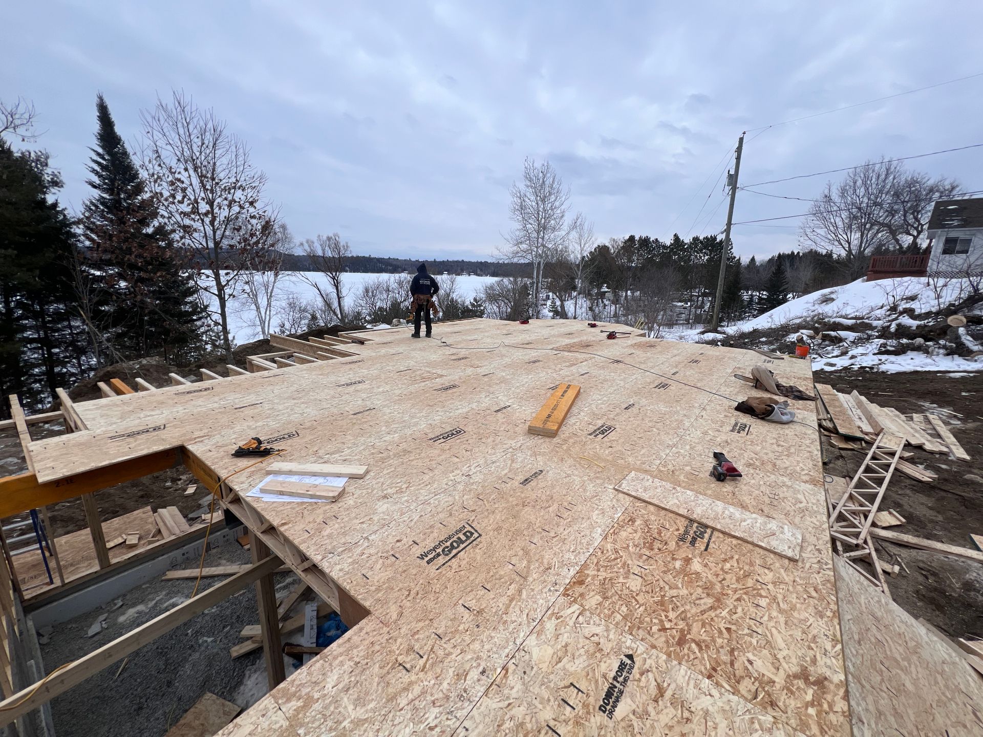Toiture en construction sur un site enneigé au bord d'un lac, avec un ouvrier au loin.