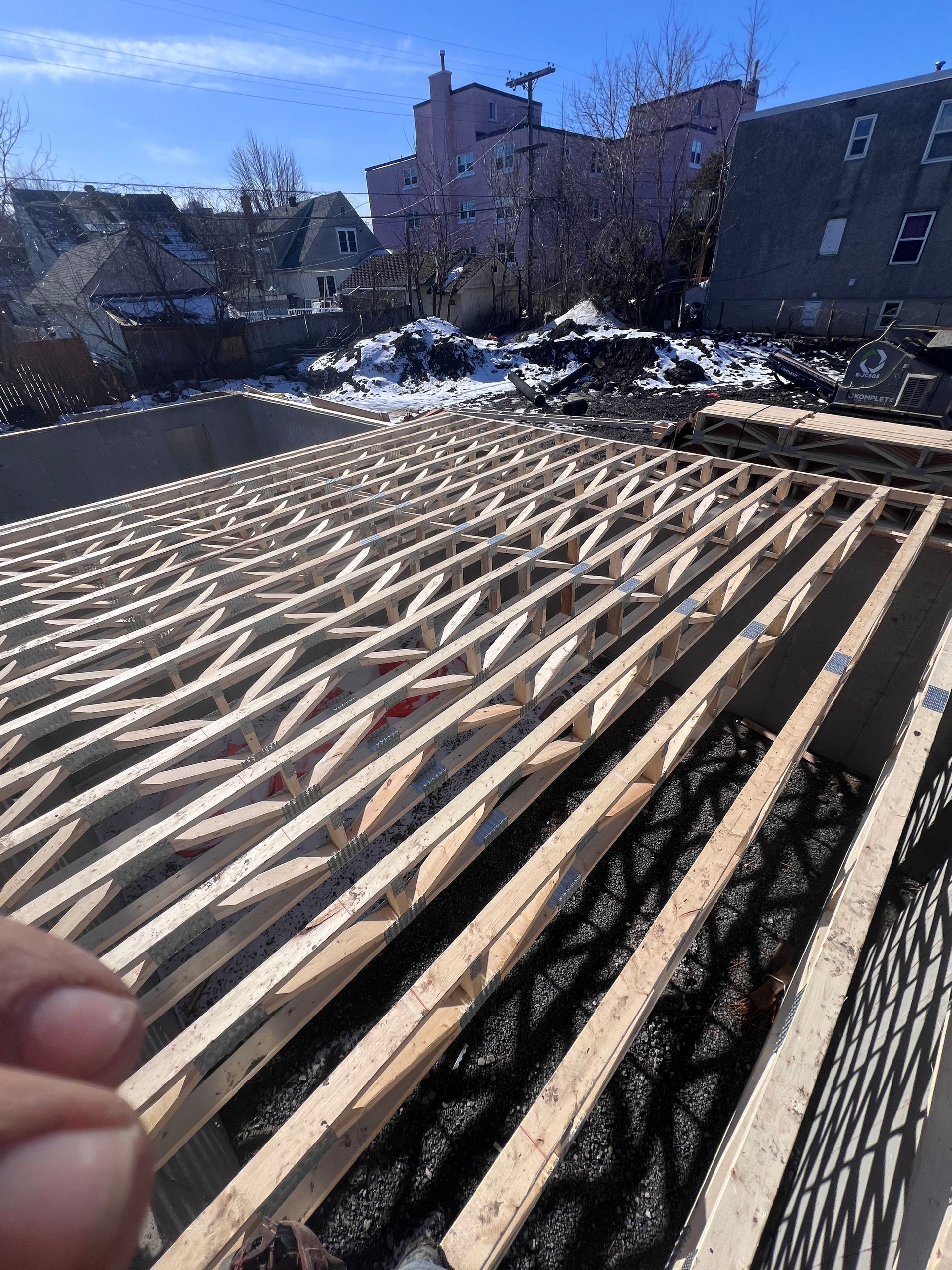 Construction d'une charpente de terrasse en bois dans une cour arrière enneigée avec des maisons en arrière-plan.