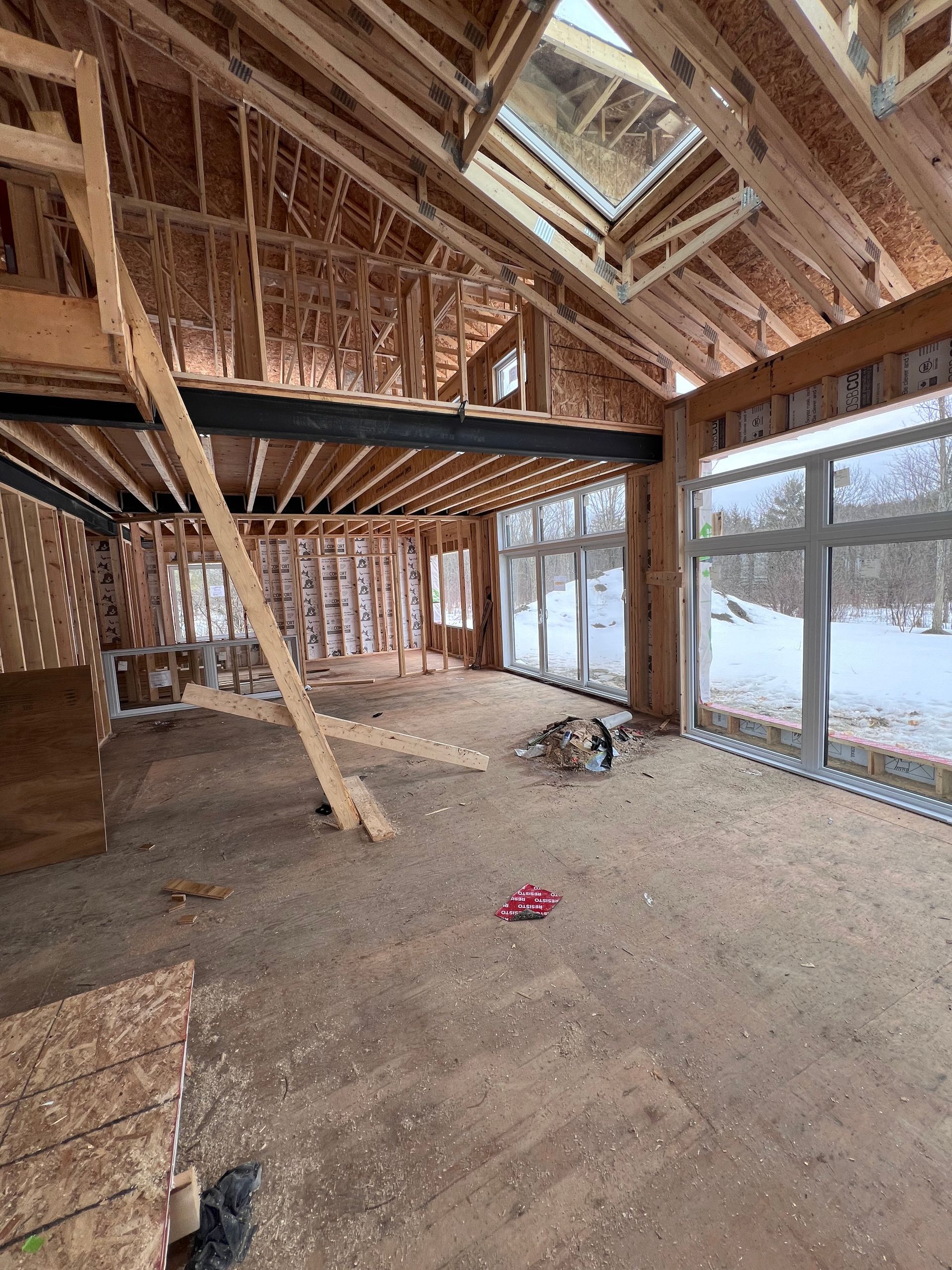 Intérieur en bois partiellement démoli, avec poutres apparentes, grandes fenêtres et débris au sol.