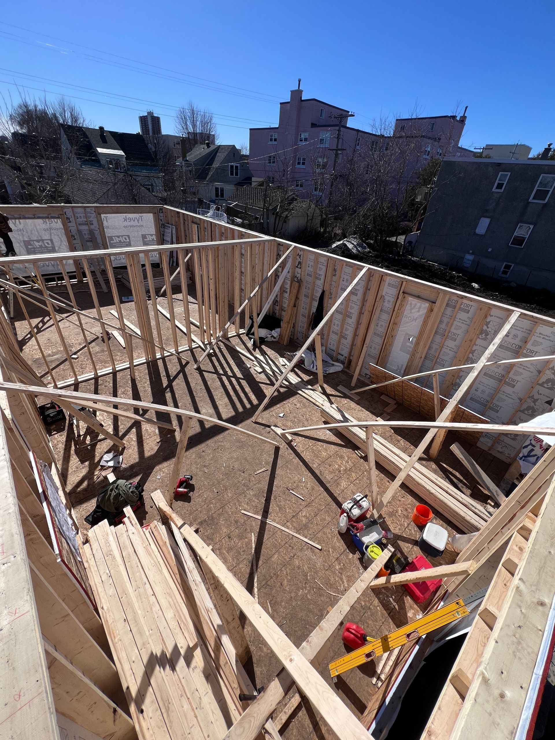 Maison partiellement en construction, avec murs en bois, solives et outils, baignée de soleil.