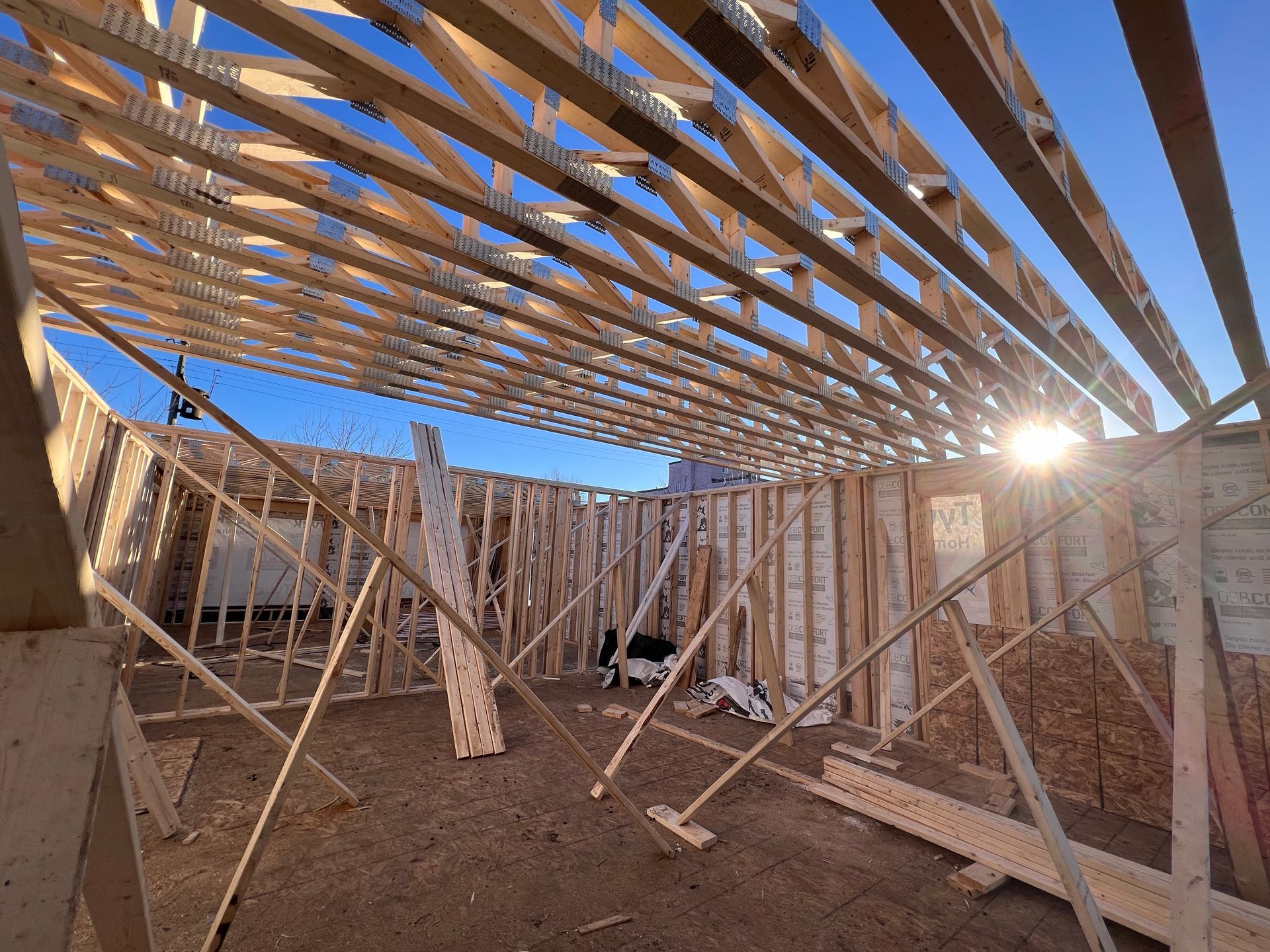 Maison partiellement à ossature bois en construction, avec charpente apparente et lumière du soleil pénétrant à travers la structure.