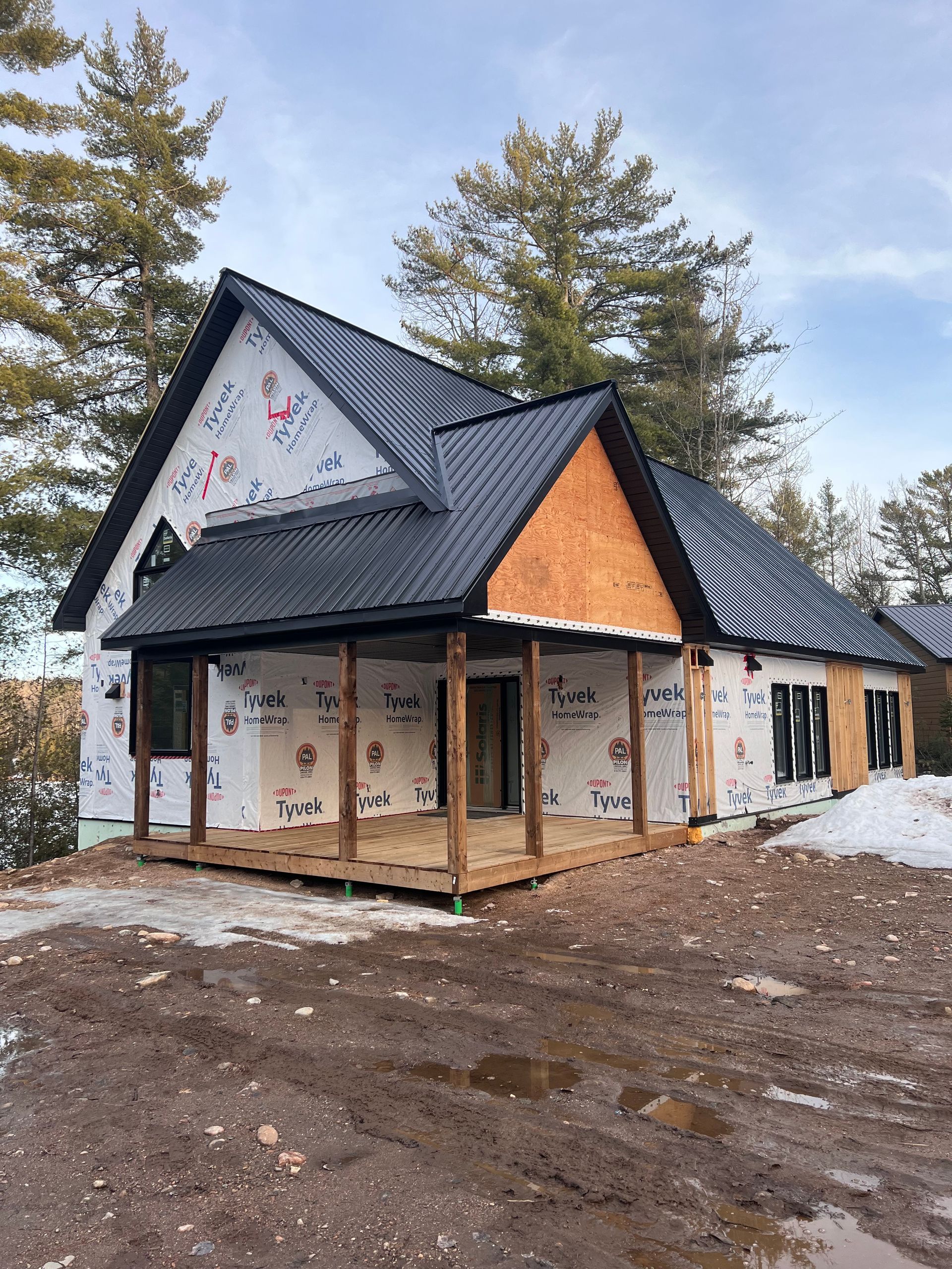 Maison partiellement construite avec toit sombre et murs blancs dans une zone boisée enneigée