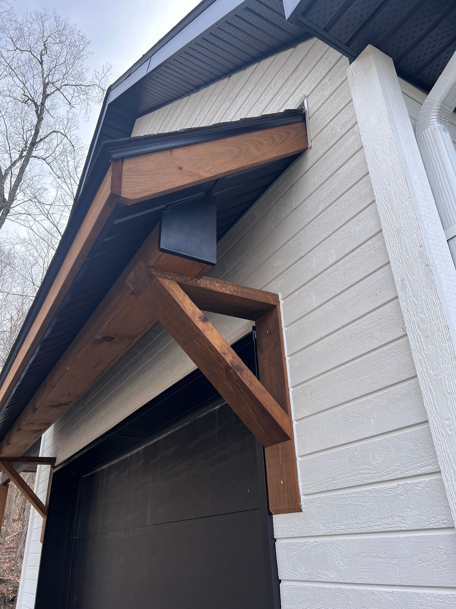 Vue extérieure d'une maison avec une porte de garage sombre et des supports en bois sous la toiture.