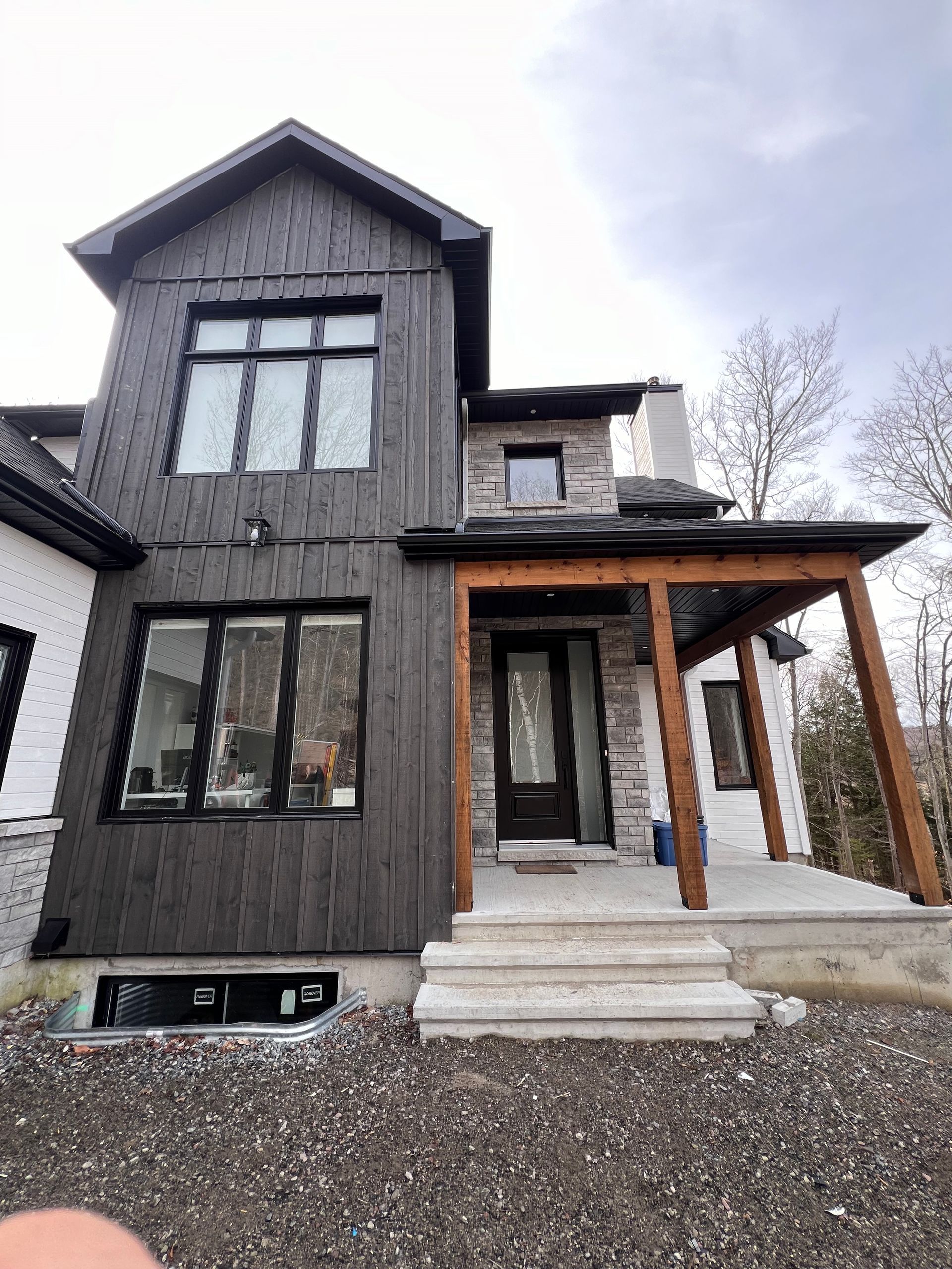 Maison moderne grise à deux étages avec poteaux de porche en bois, marches d'entrée et cour en gravier