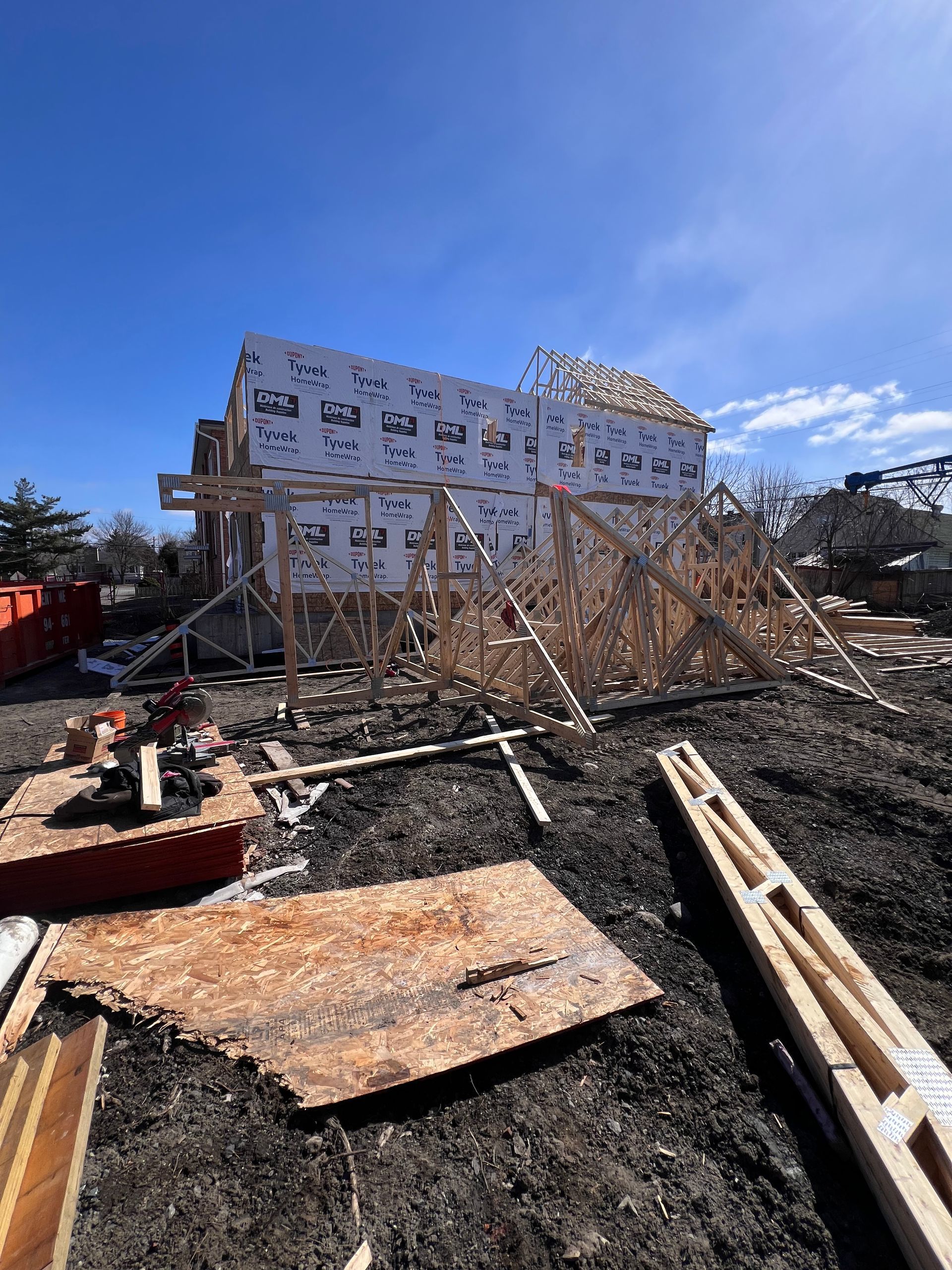 Maison endommagée en construction, avec des débris et une charpente apparente sous un ciel bleu