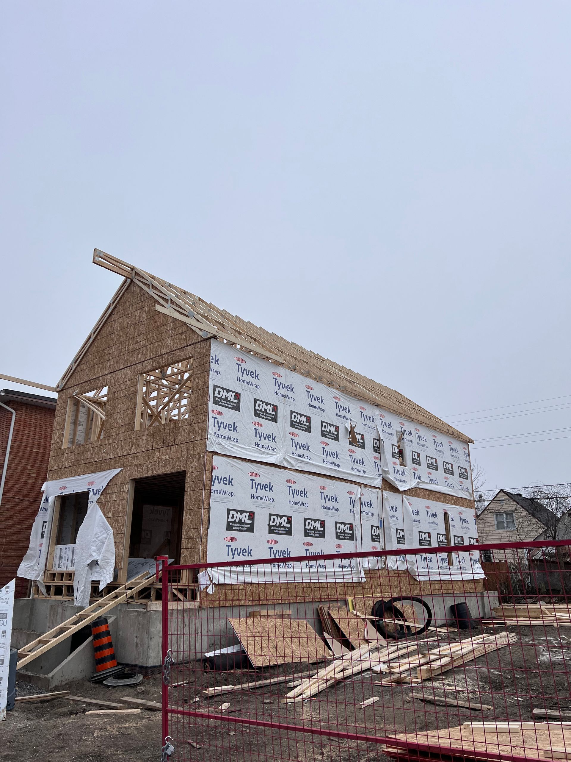 Maison partiellement finie en construction avec échafaudages, revêtement extérieur et débris devant.