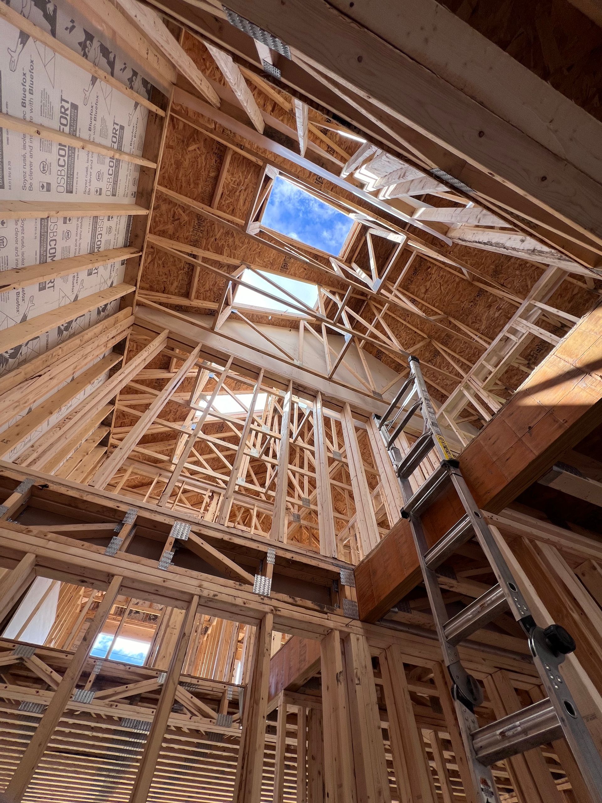 Intérieur d'une maison à ossature bois en construction, avec chevrons, montants et ouverture de puits de lumière apparents.