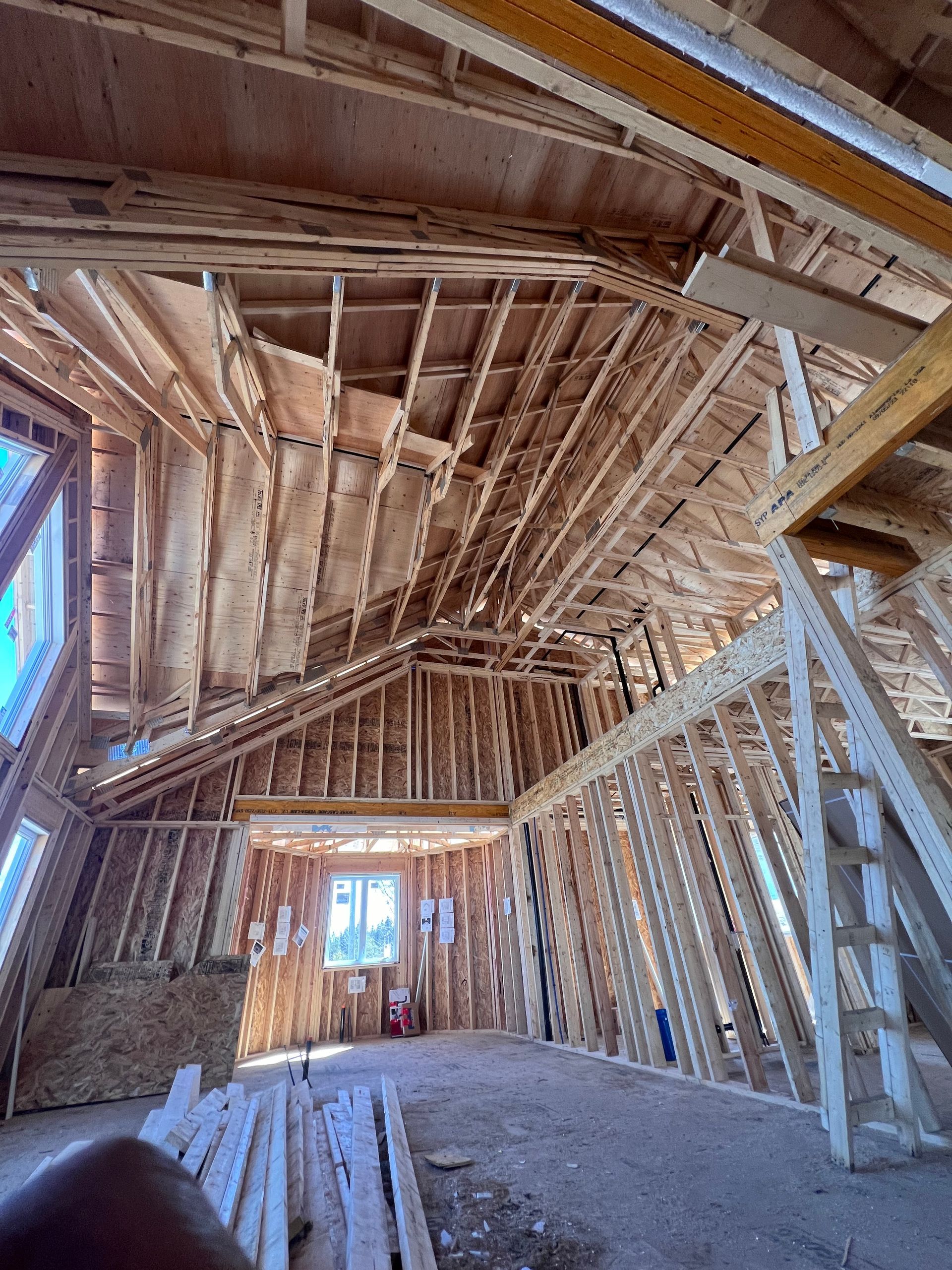 Intérieur d'une pièce en bois inachevée, avec charpente apparente et plafond incliné, en cours de construction.