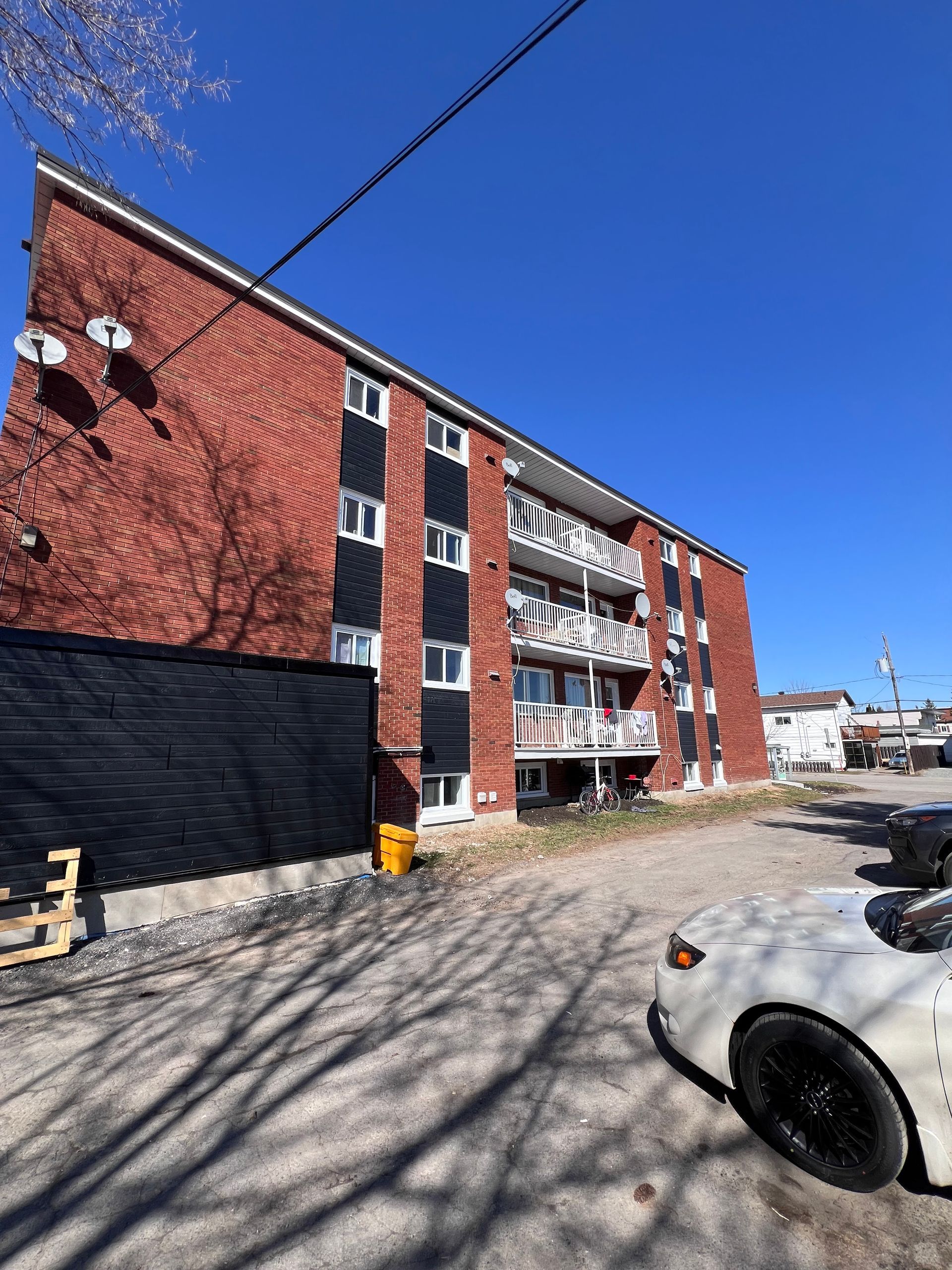 Immeuble d'appartements en briques par une journée ensoleillée, avec des voitures garées et une rue enneigée à proximité