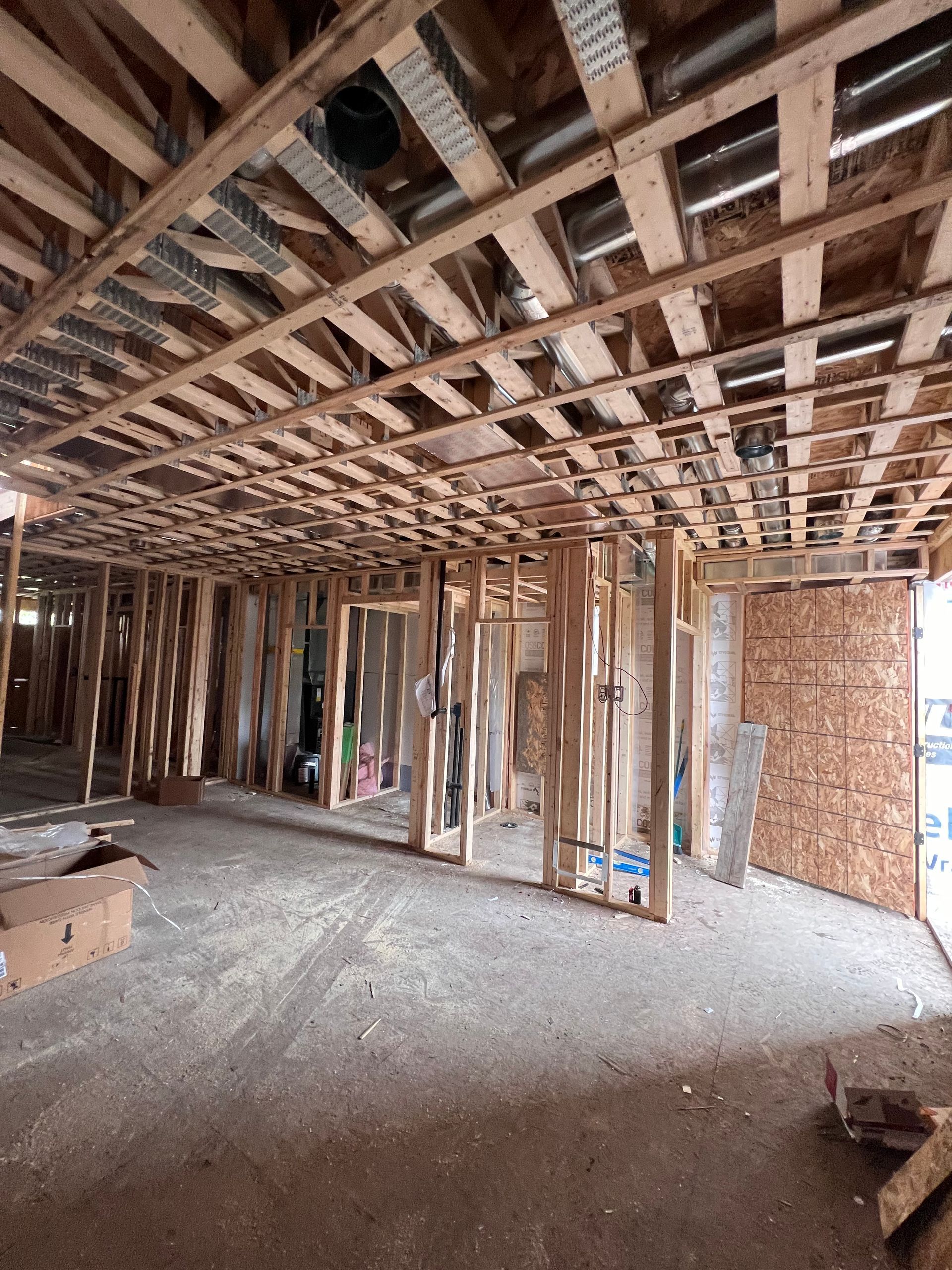 Charpente apparente en bois et murs inachevés à l'intérieur d'un chantier de construction, avec des débris au sol.