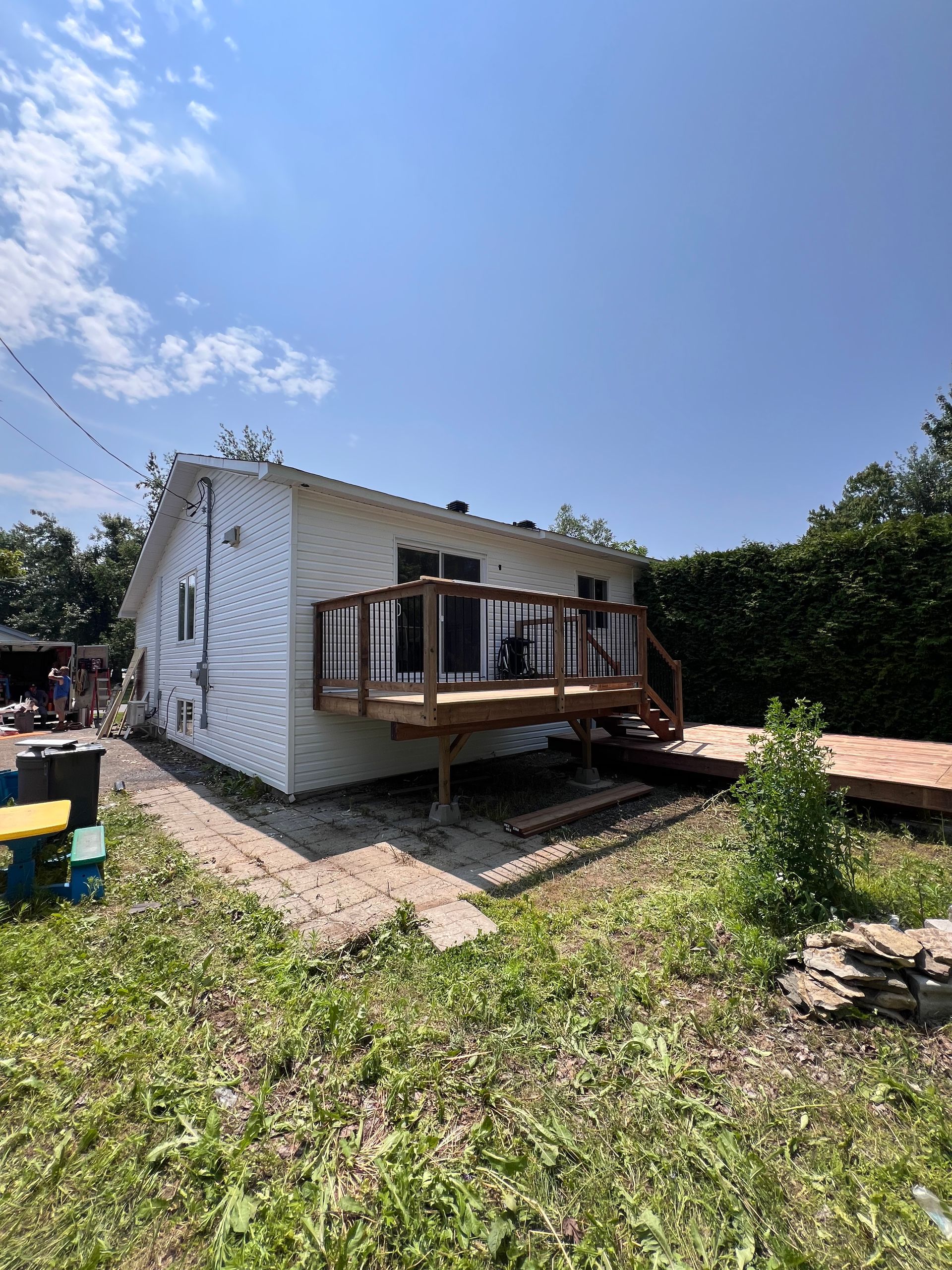 Petite cabane blanche avec une terrasse en bois dans une cour herbeuse sous un ciel d'un bleu éclatant