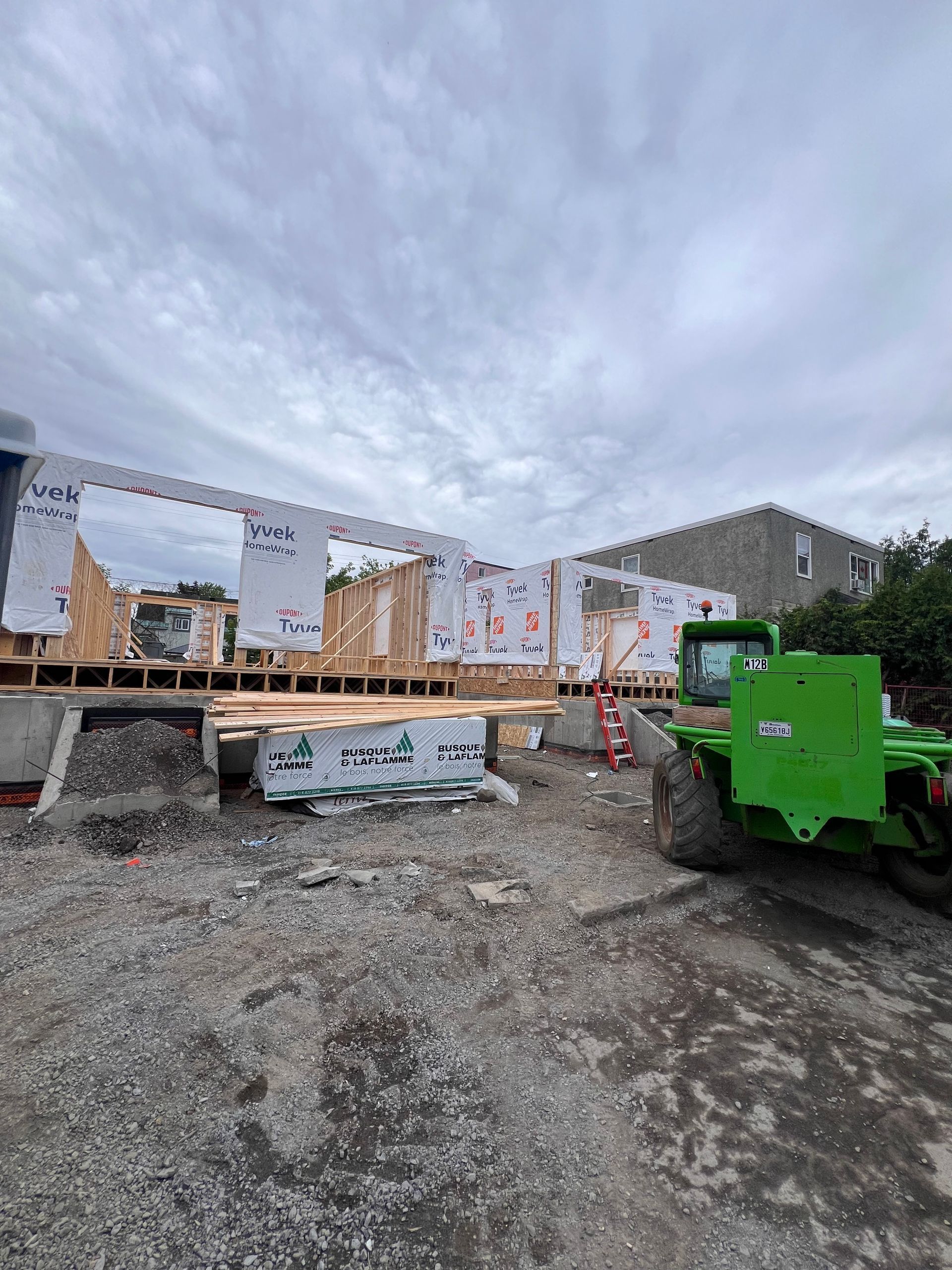 Chantier de construction avec une structure en bois surélevée, des engins verts et un ciel couvert