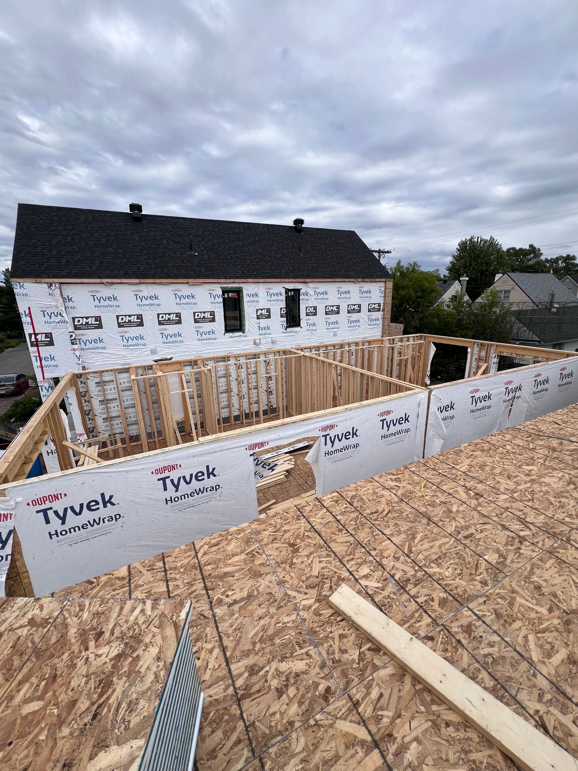 Maison partiellement construite, ossature bois avec revêtement OSB et membrane Tyvek, sous un ciel nuageux