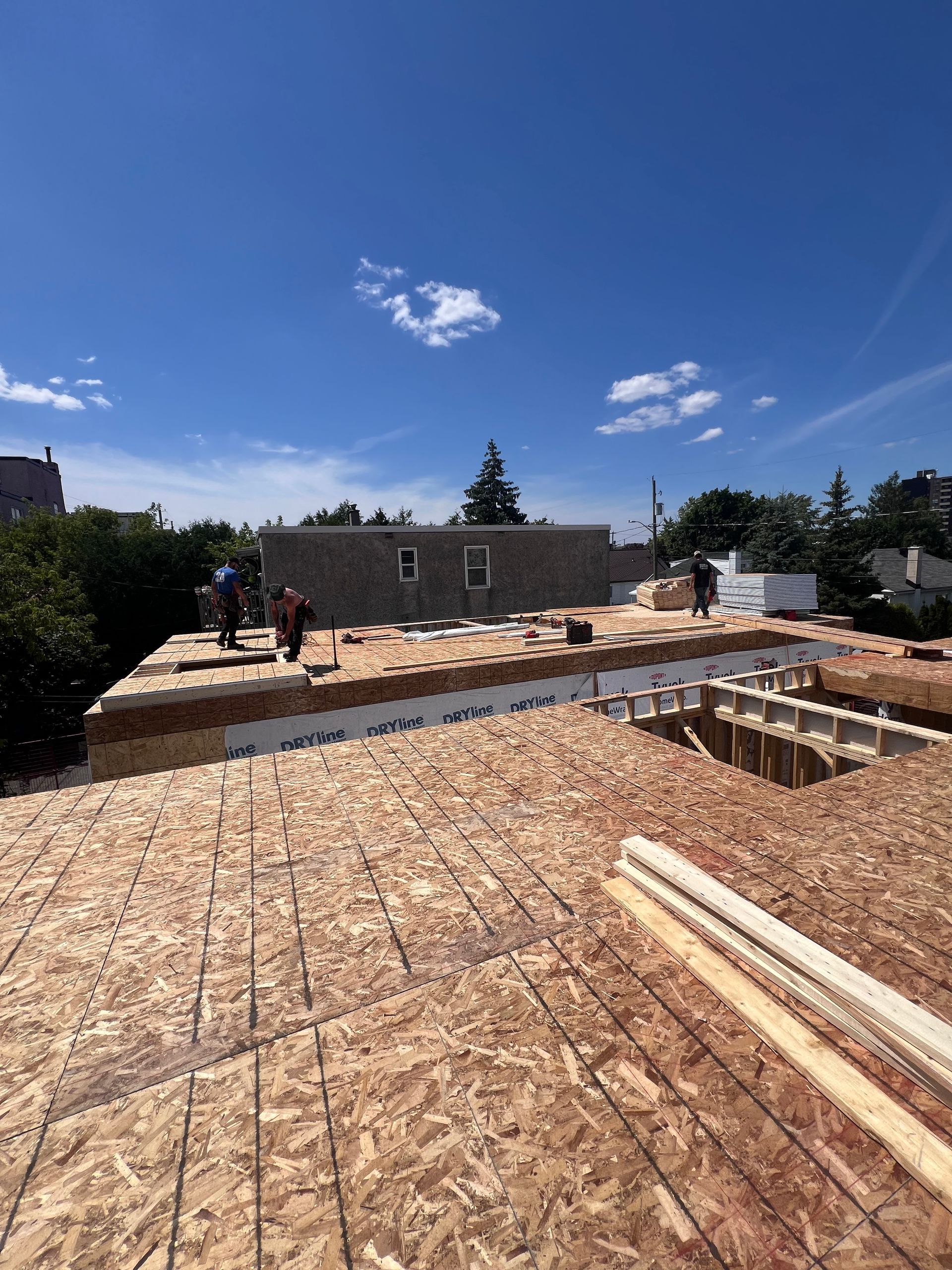 Chantier de construction avec sol en contreplaqué et murs partiellement construits sous un ciel d'un bleu éclatant