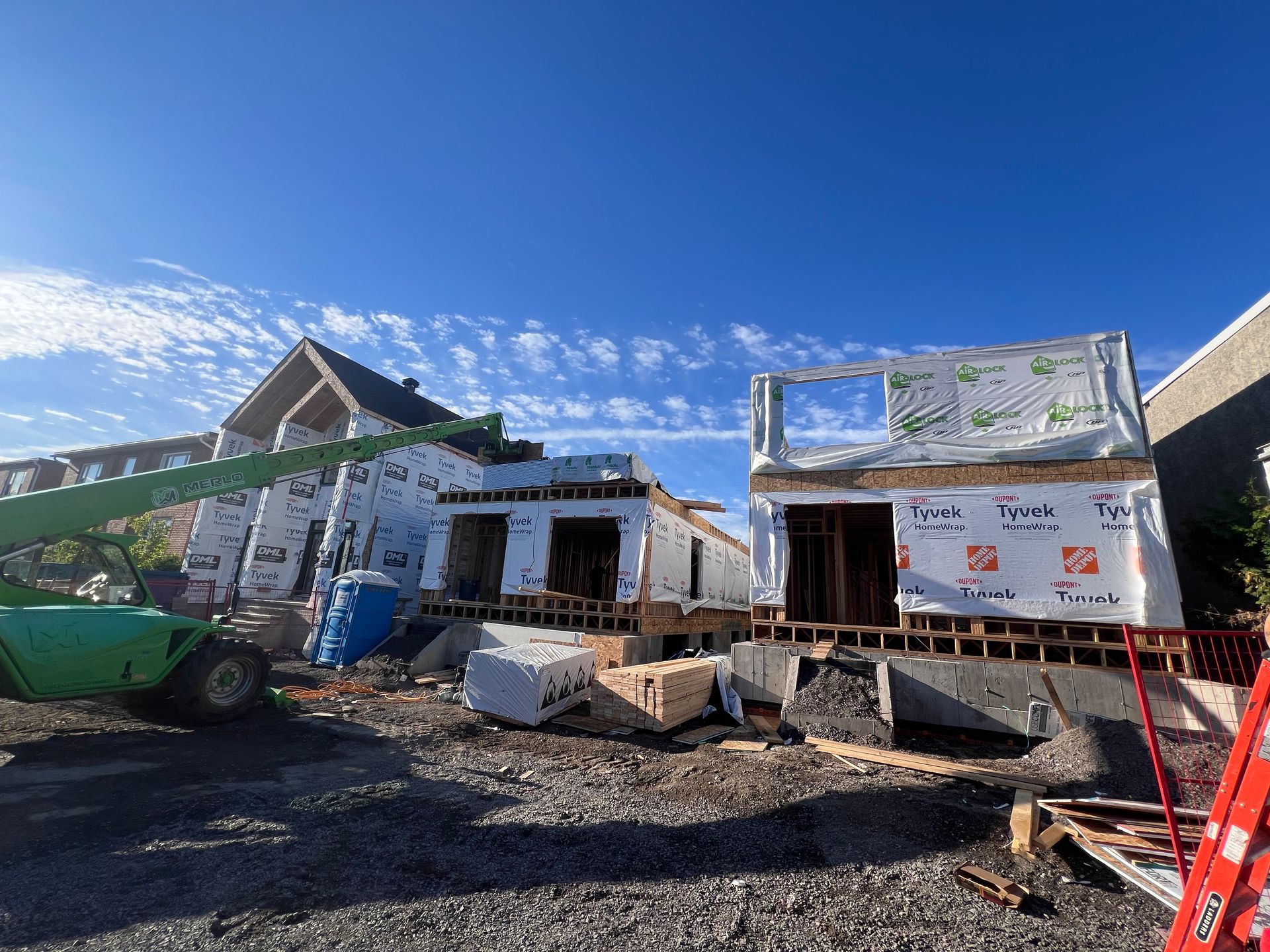 Chantier de construction avec des bâtiments blancs inachevés, des machines vertes et des débris sous un ciel bleu