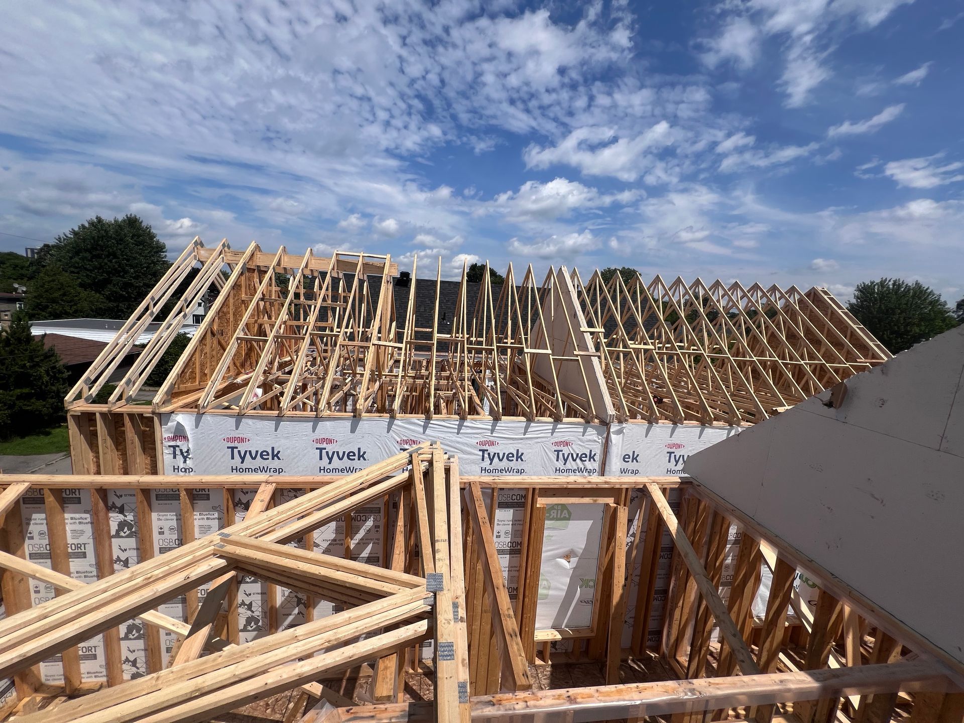Ossature bois d'une maison partiellement construite sous un ciel bleu nuageux