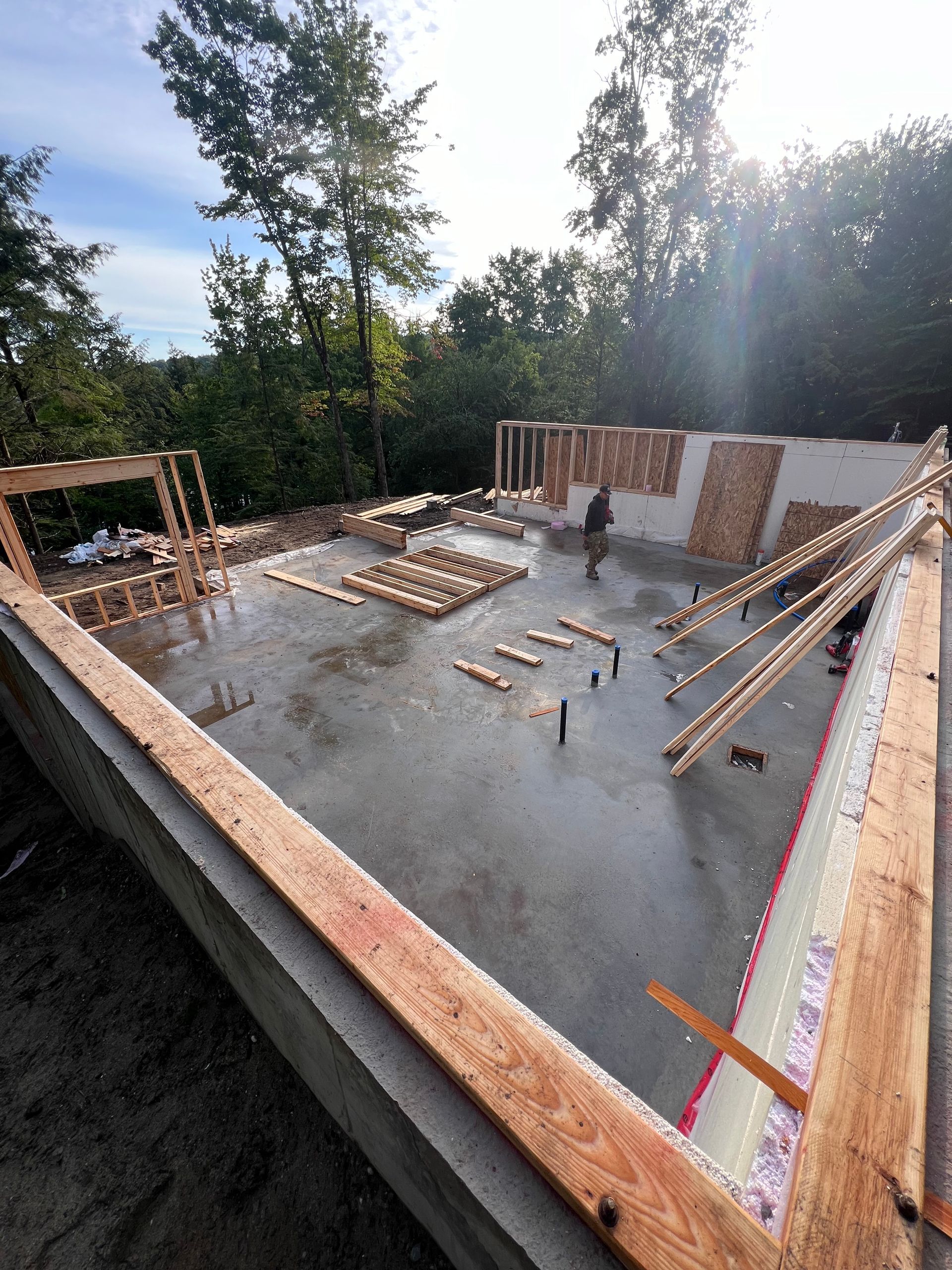 Fondations en béton en construction avec ossature bois, armatures métalliques et un ouvrier à l'extérieur au coucher du soleil.