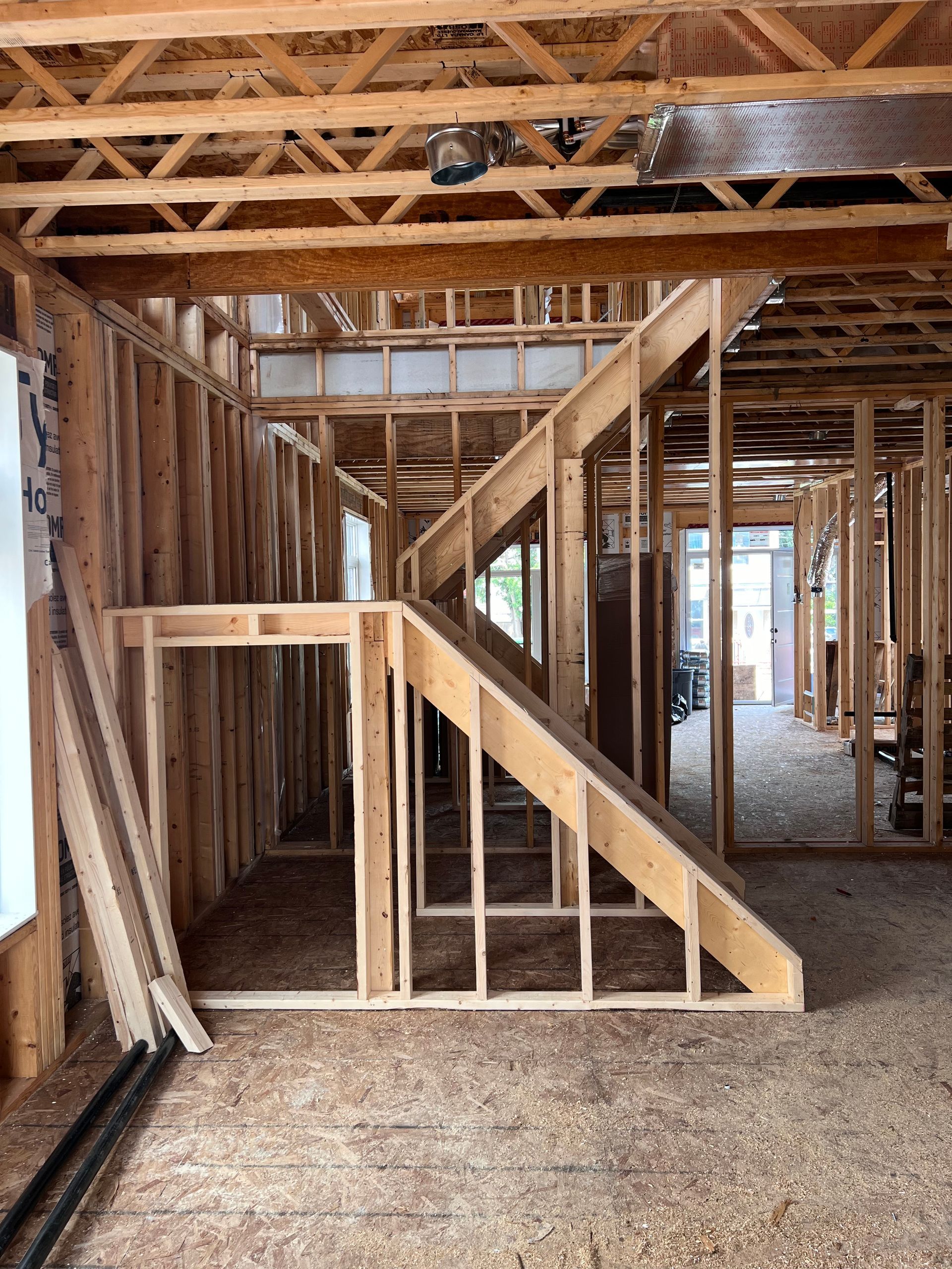 Intérieur d'une maison en construction avec charpente apparente en bois et structure de la cage d'escalier.