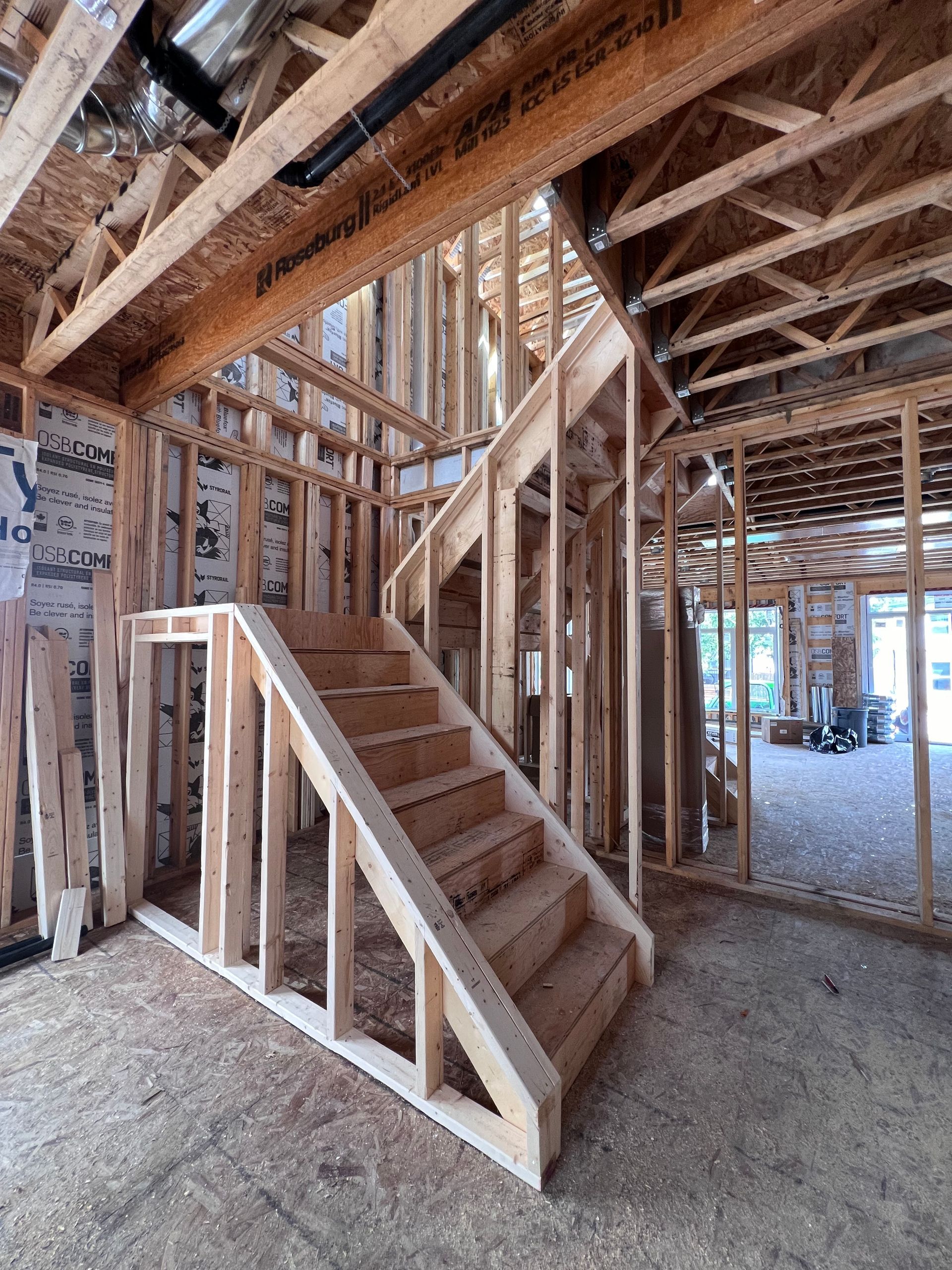 Escalier à ossature bois à l'intérieur d'une maison en construction, avec poutres apparentes et murs inachevés.