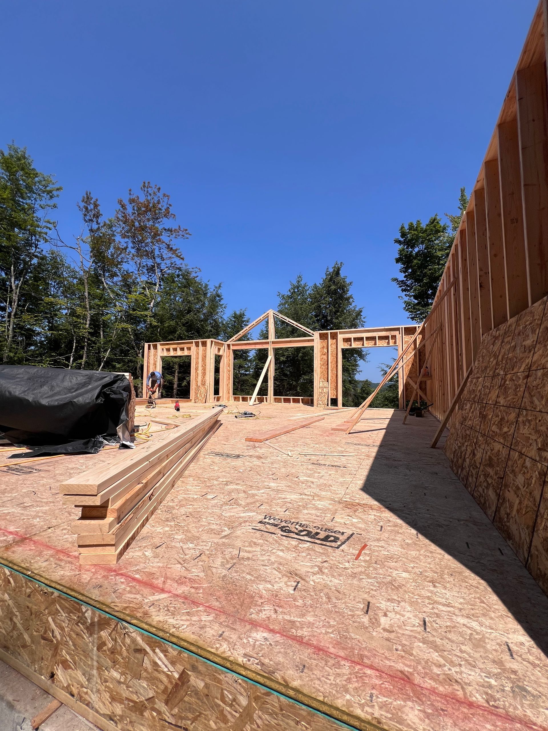 Ossature bois partiellement construite d'une maison sur un terrain vague sous un ciel bleu