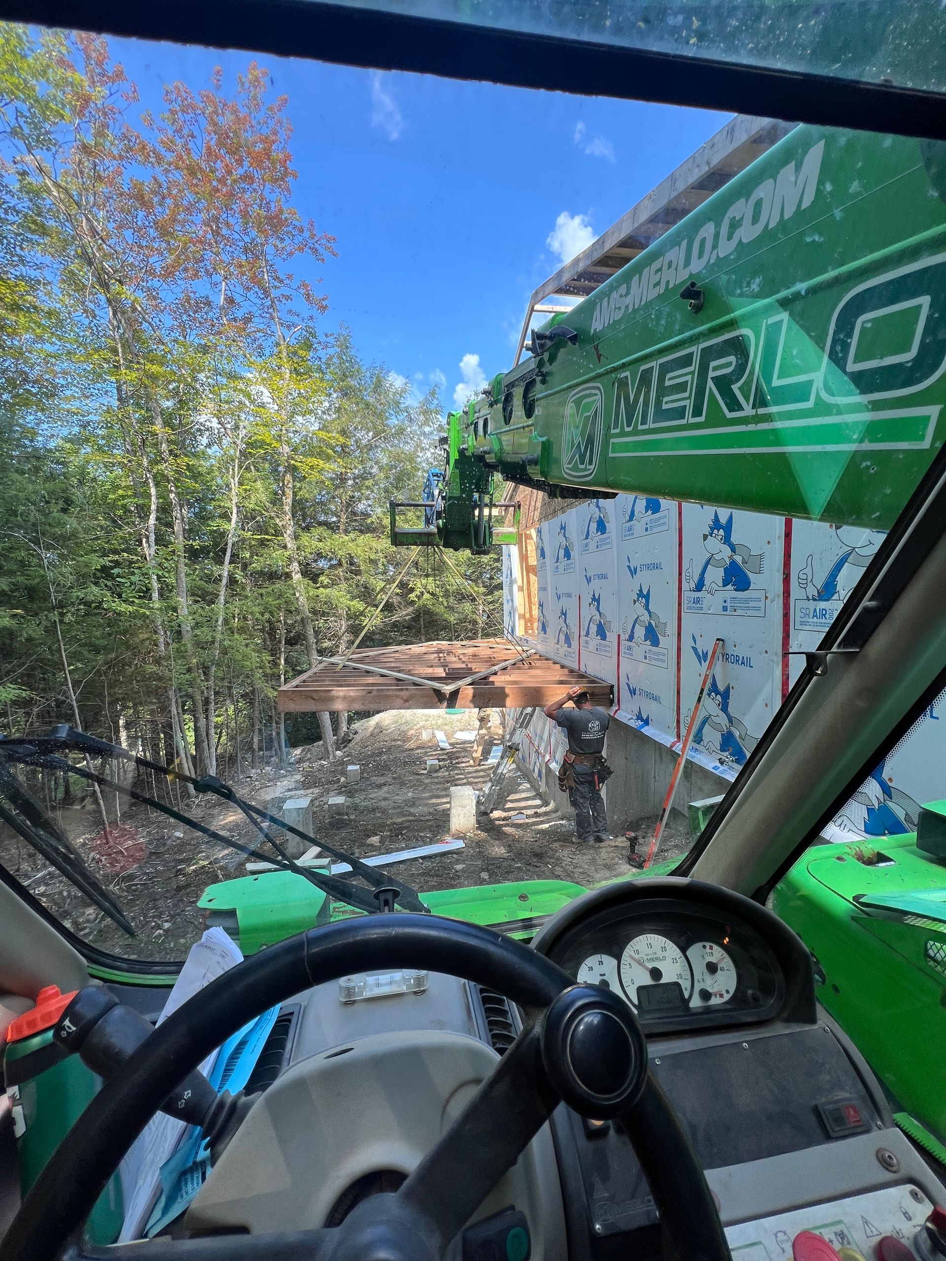 À l'intérieur de la cabine d'un véhicule vert, la vue donne sur une cour boisée avec une table de pique-nique et un ciel bleu.