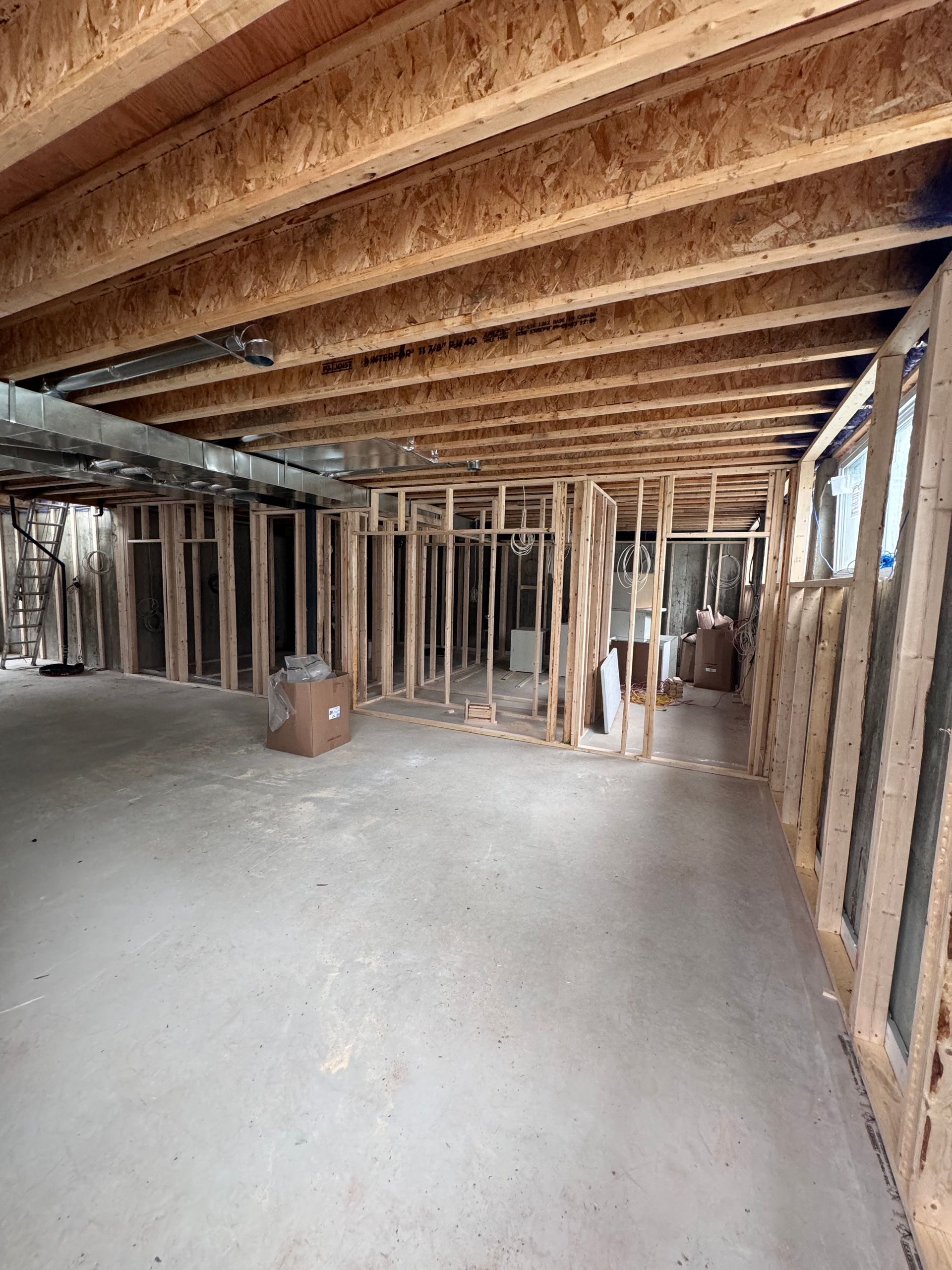 Pièce en construction, inachevée, avec poutres et montants en bois apparents, et sol en béton.