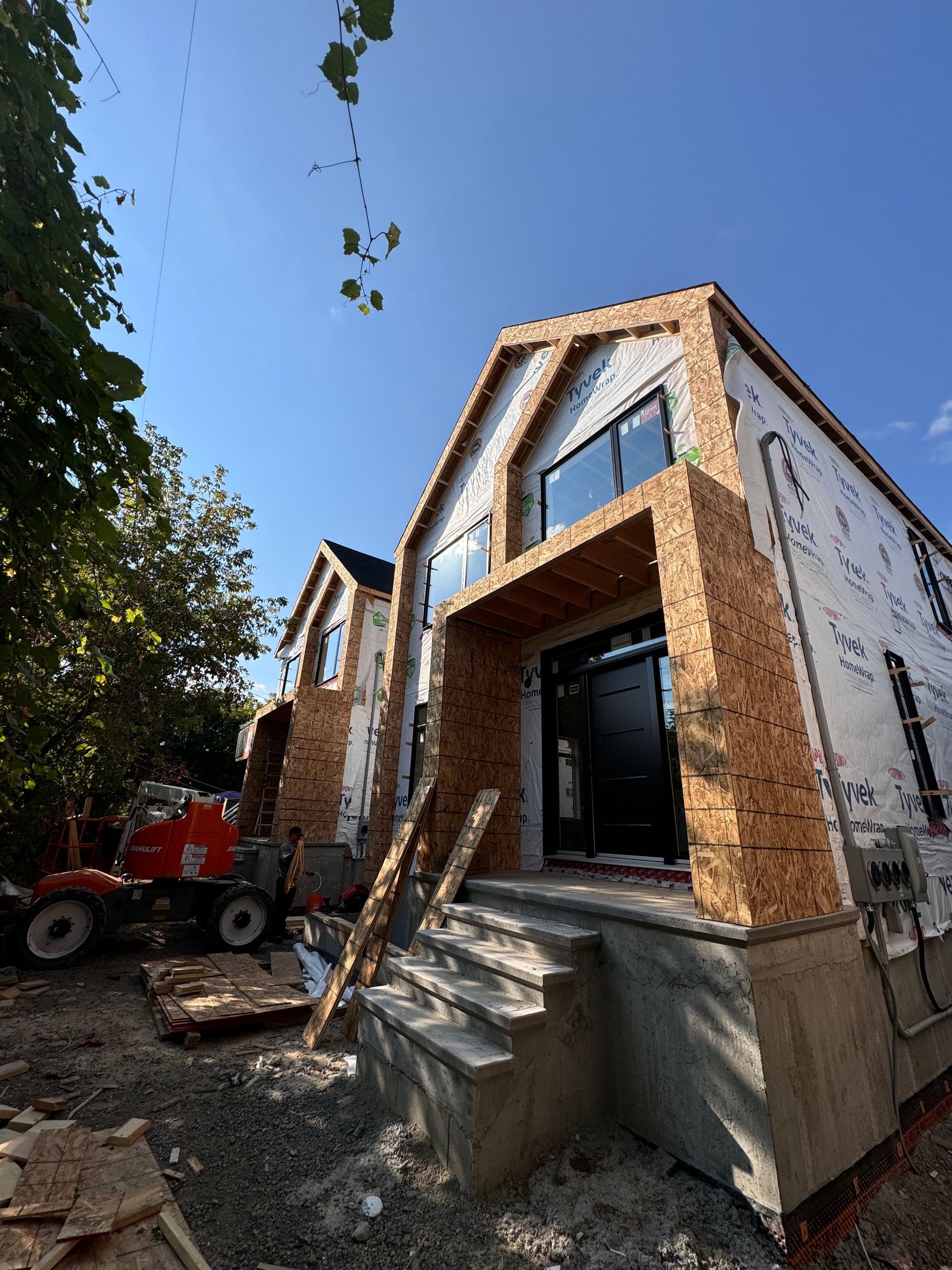 Maison en briques en construction avec perron, grandes fenêtres et un tracteur rouge à proximité