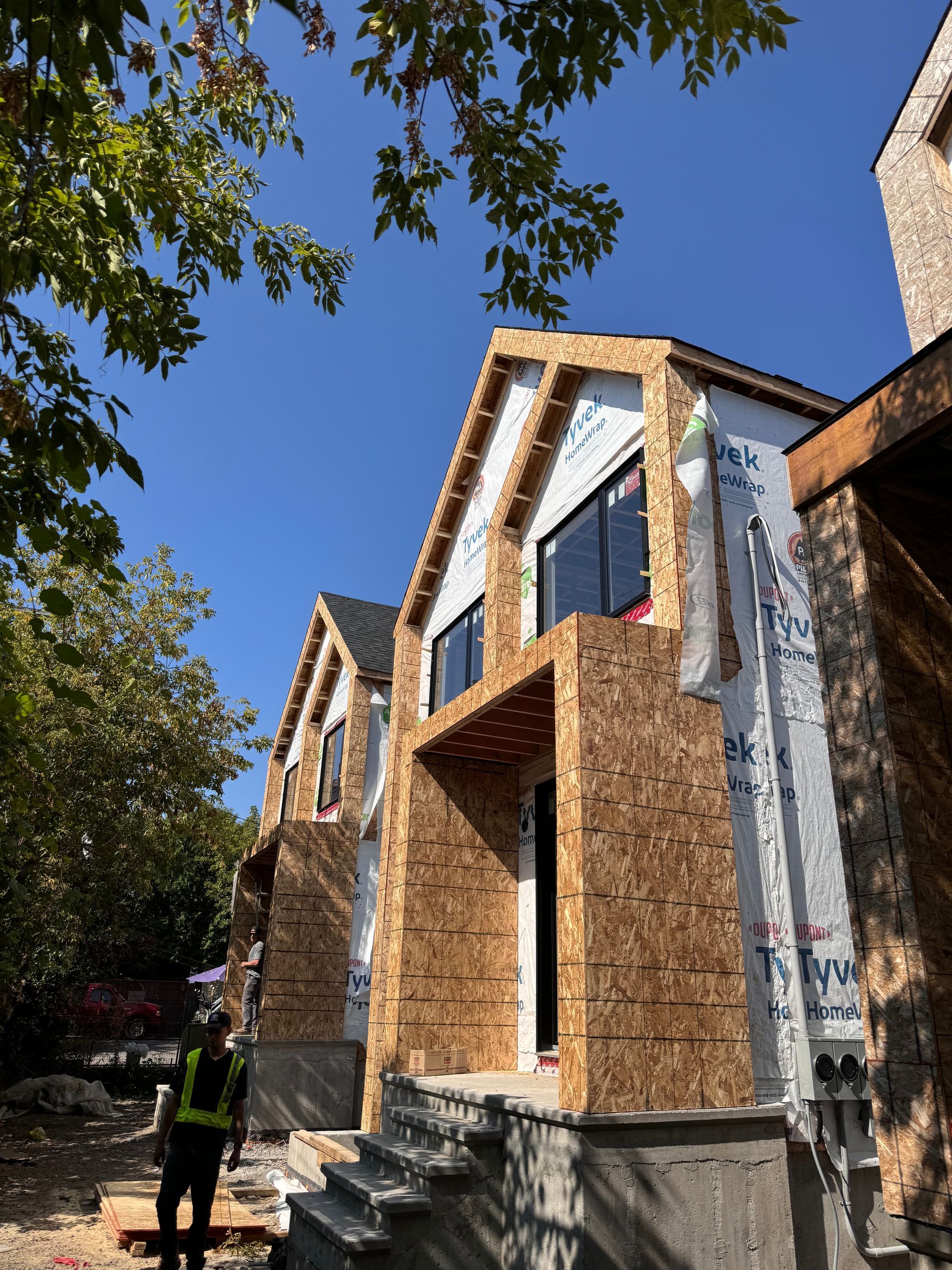Un bâtiment sombre et moderne en construction, avec des fenêtres en verre et une nacelle élévatrice rouge garée devant, se détachant sur un ciel enneigé.