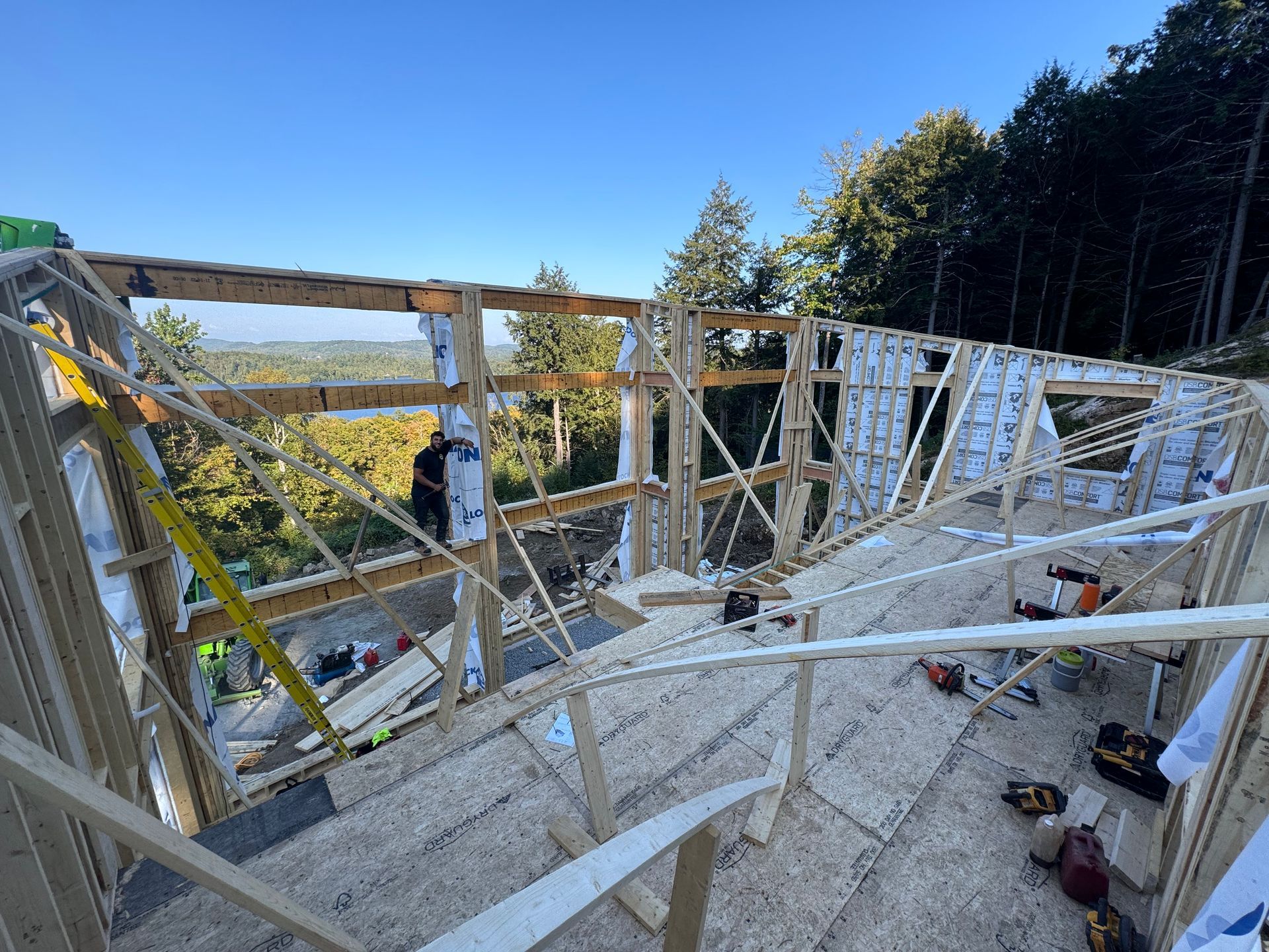 Bâtiment en construction, partiellement ossature bois, avec des murs en bois blanc et une vue sur les champs verdoyants au-delà.