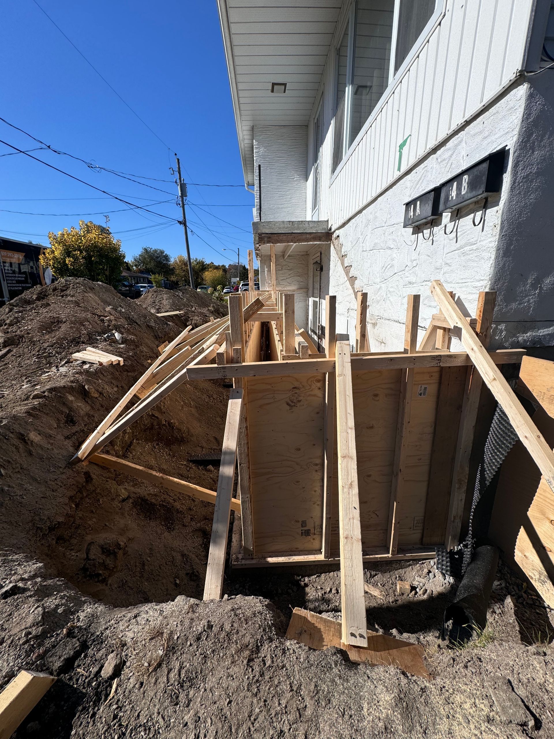 Coffrage et étais en bois à côté des fondations d'une maison sur un chantier de construction en terre battue, sous un ciel bleu.