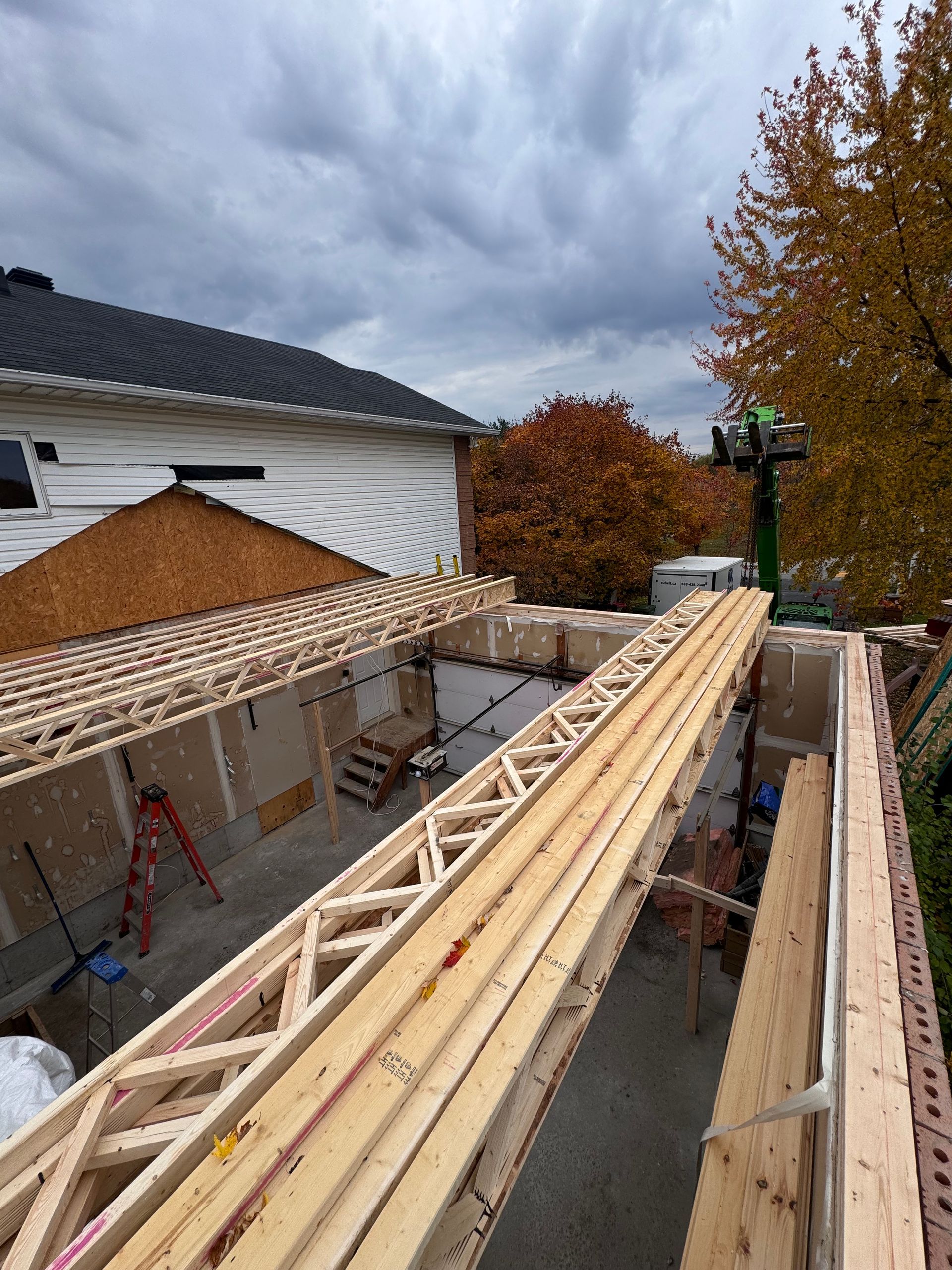 Installation de la charpente d'une extension de maison sous un ciel nuageux.