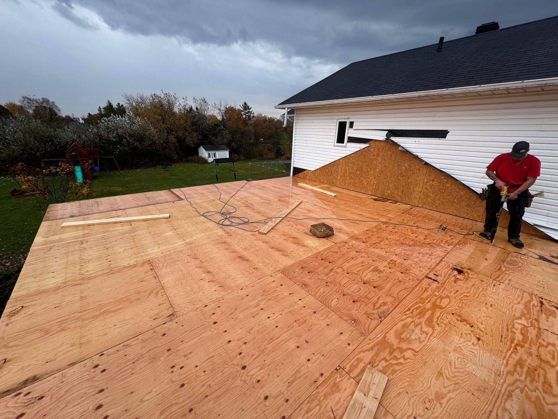 Des ouvriers installent une toiture en contreplaqué sur une maison sous un ciel nuageux.