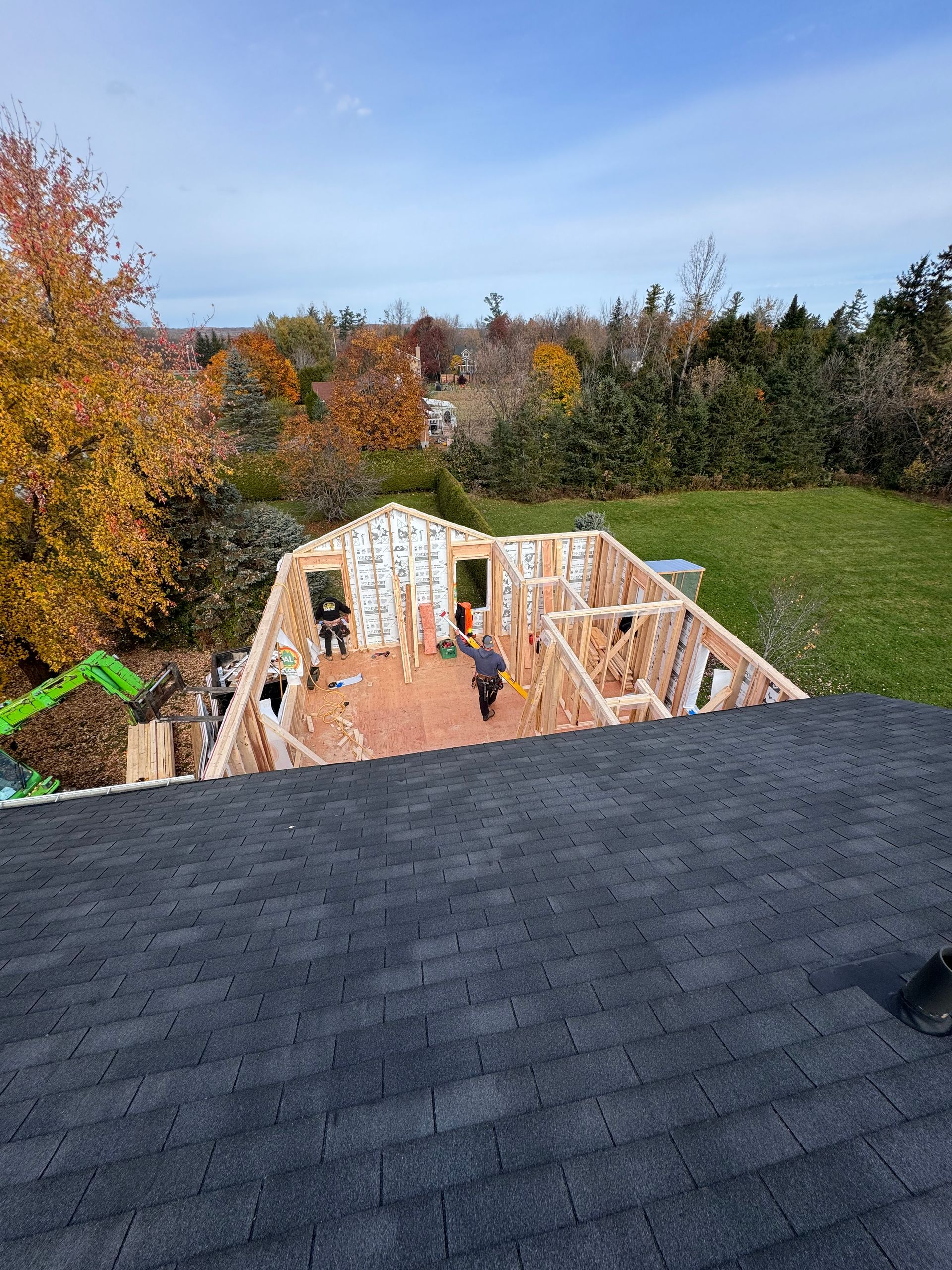 Maison en construction, vue depuis un toit de bardeaux avec des arbres d'automne en arrière-plan.
