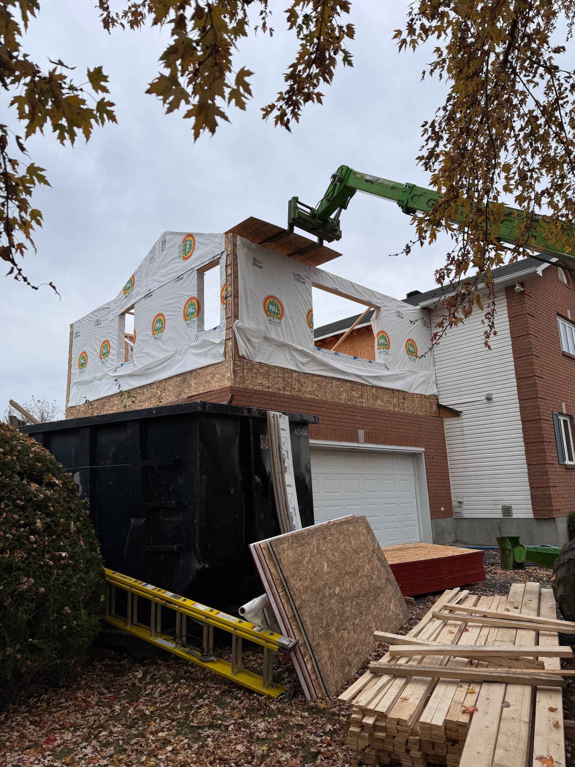 Maison en cours de démolition : une grue enlève le toit, les débris et les planches de bois devant la maison.