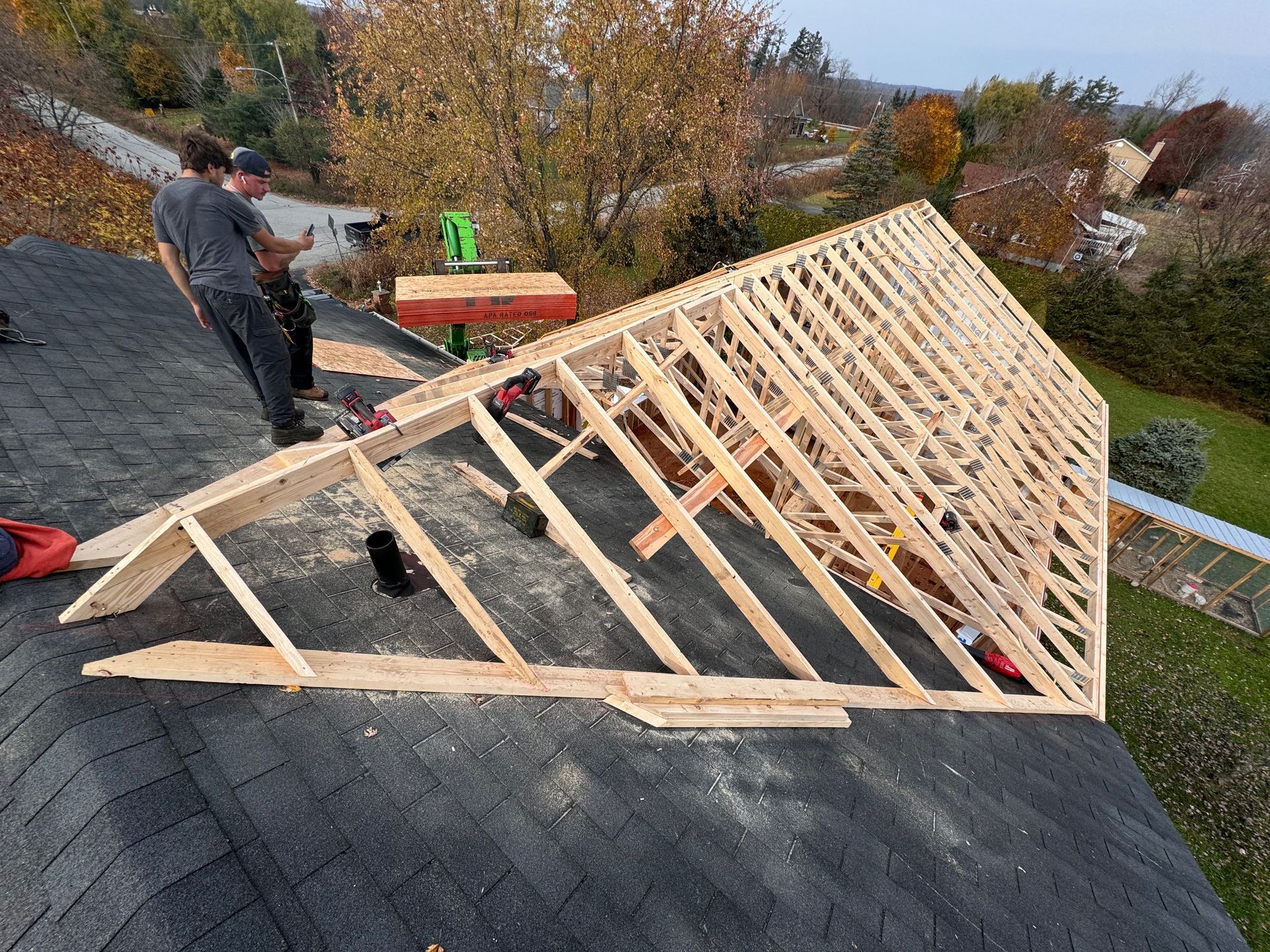 Deux ouvriers construisent la charpente d'un toit en bois sur une maison en construction recouverte de bardeaux.
