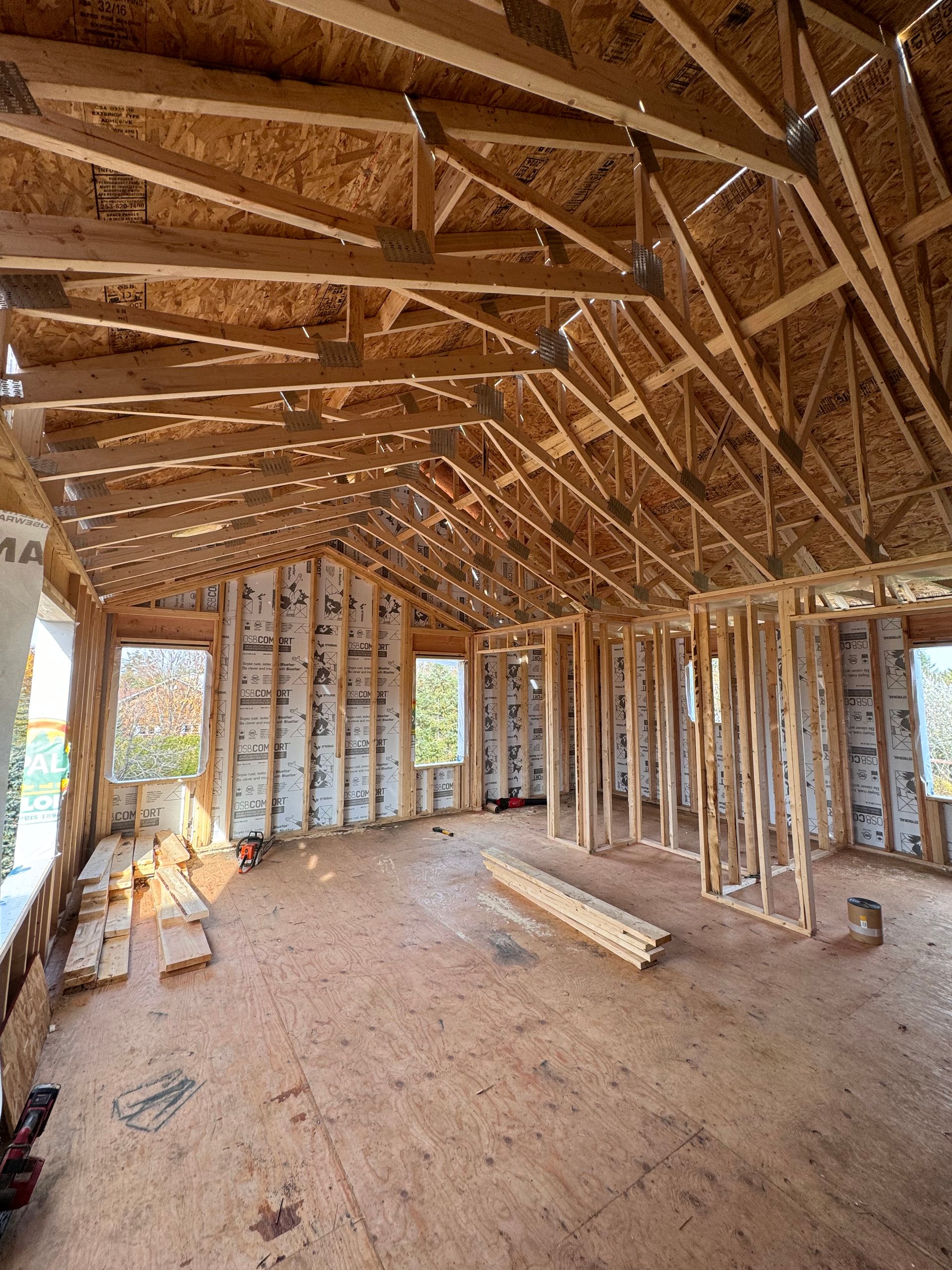 Intérieur d'une maison en bois inachevé, avec charpente apparente, montants muraux et débris de construction au sol.