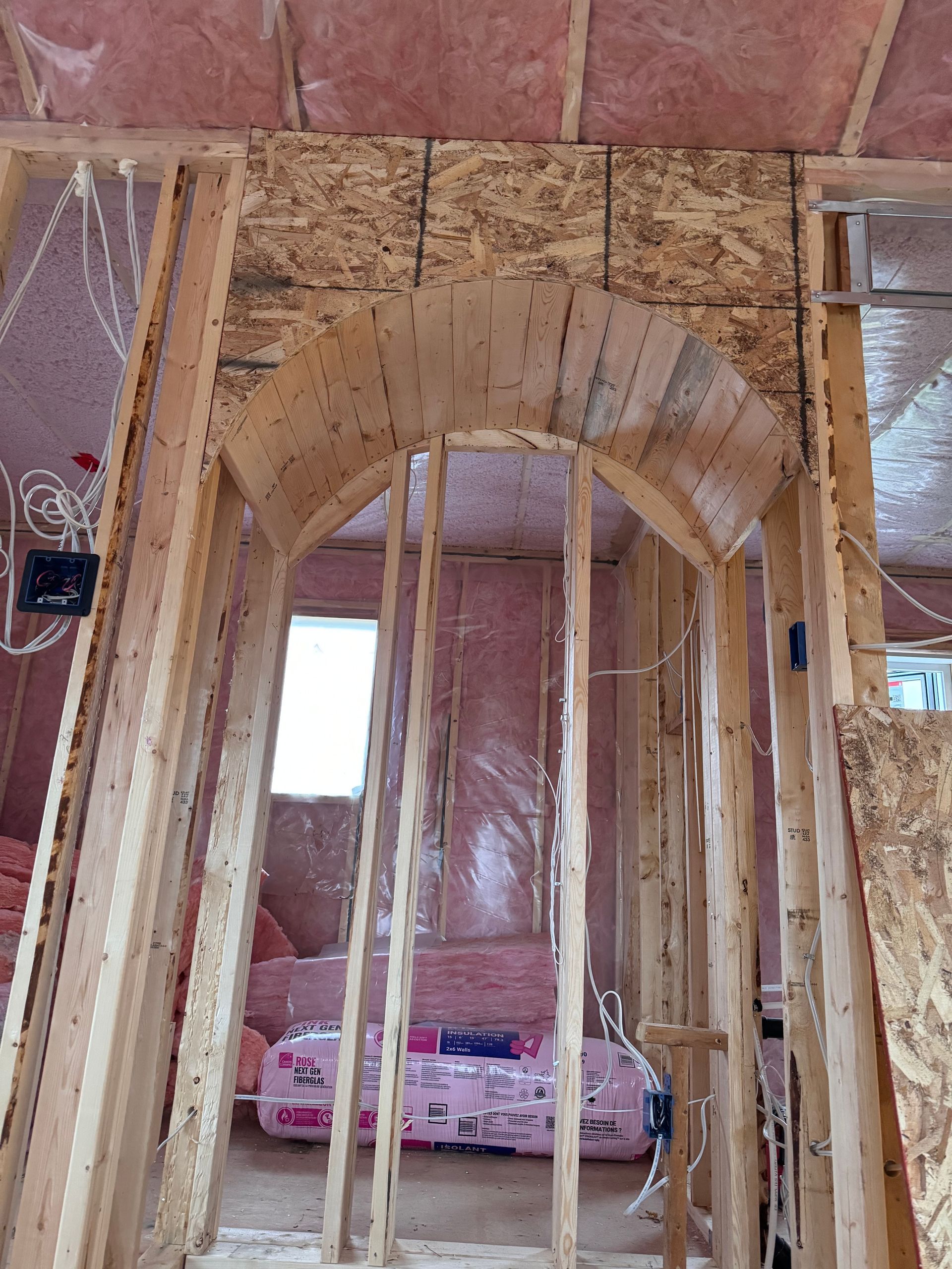 Ossature intérieure inachevée avec une porte cintrée en bois en cours de construction.
