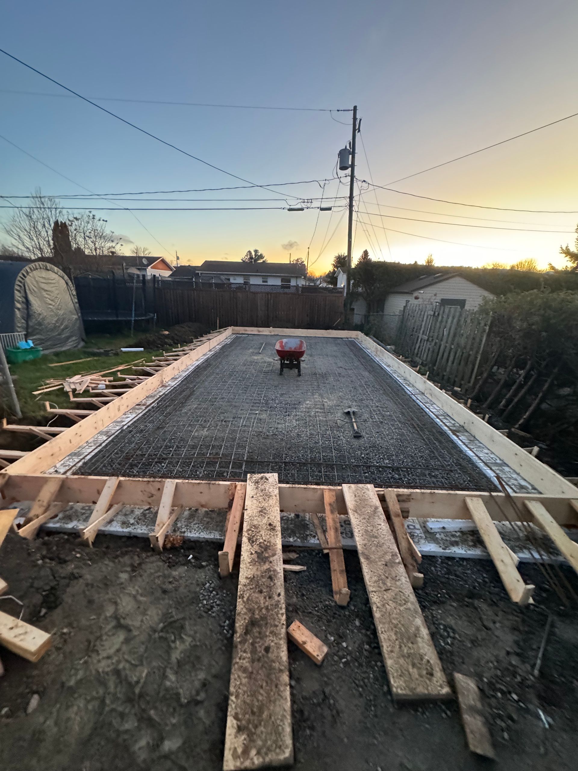 Chantier de construction dans une cour arrière avec dalle de gravier et coffrage en bois au coucher du soleil