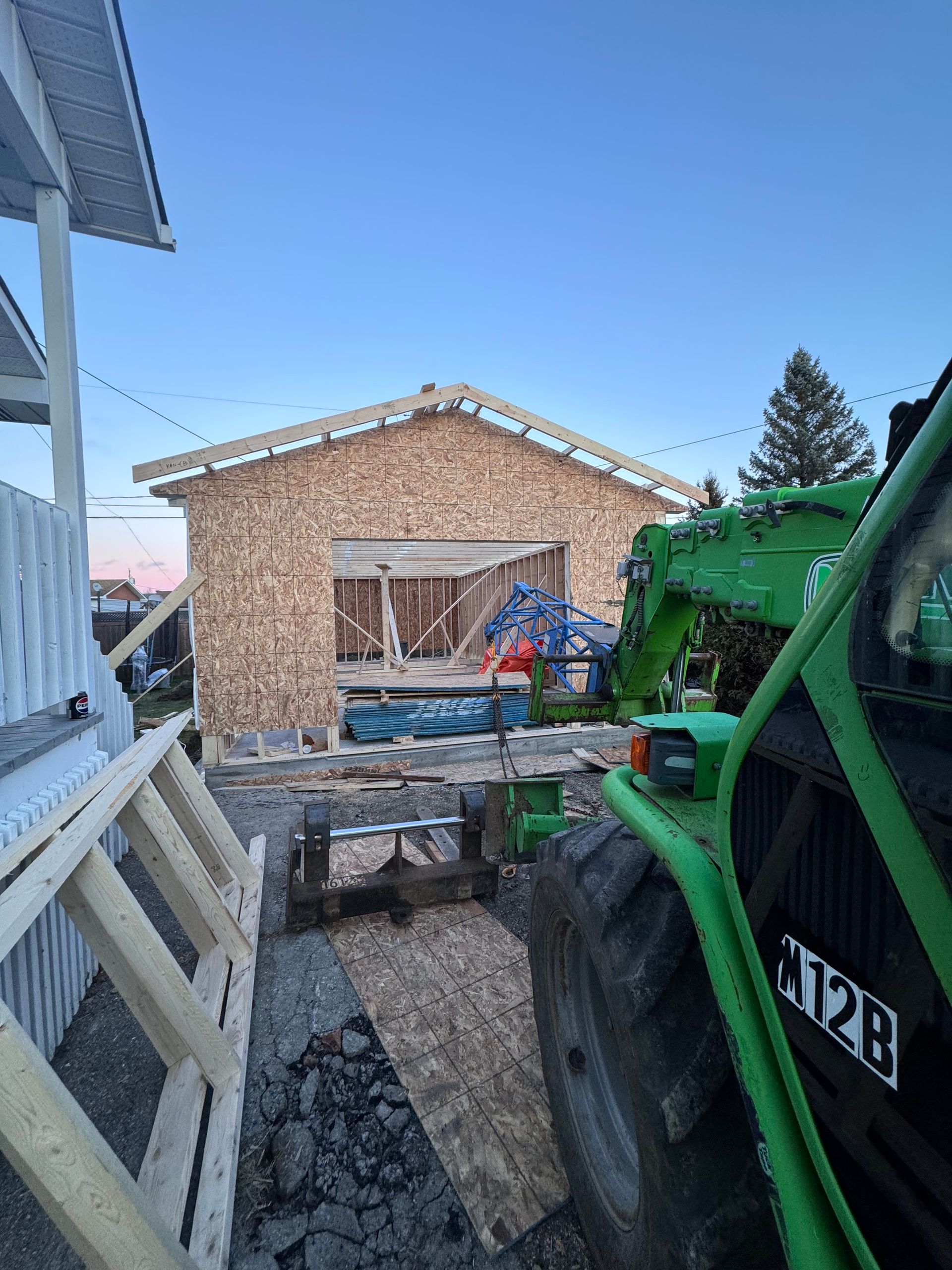 Matériel de chantier à côté d'un hangar en bois, avec un tracteur vert au premier plan.
