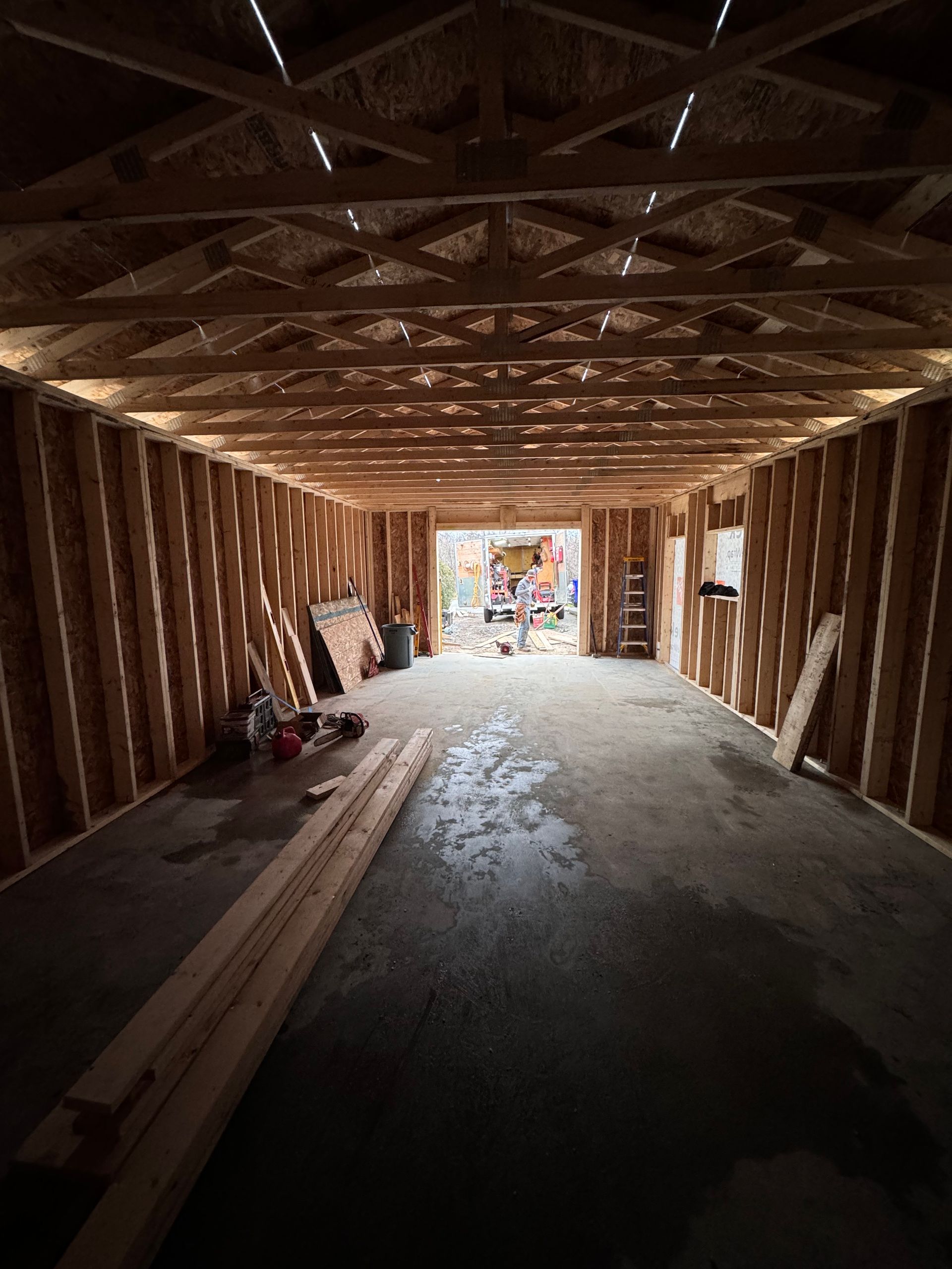 Intérieur d'une structure en bois inachevée avec poutres, sol en béton et lumière du jour à l'ouverture du fond