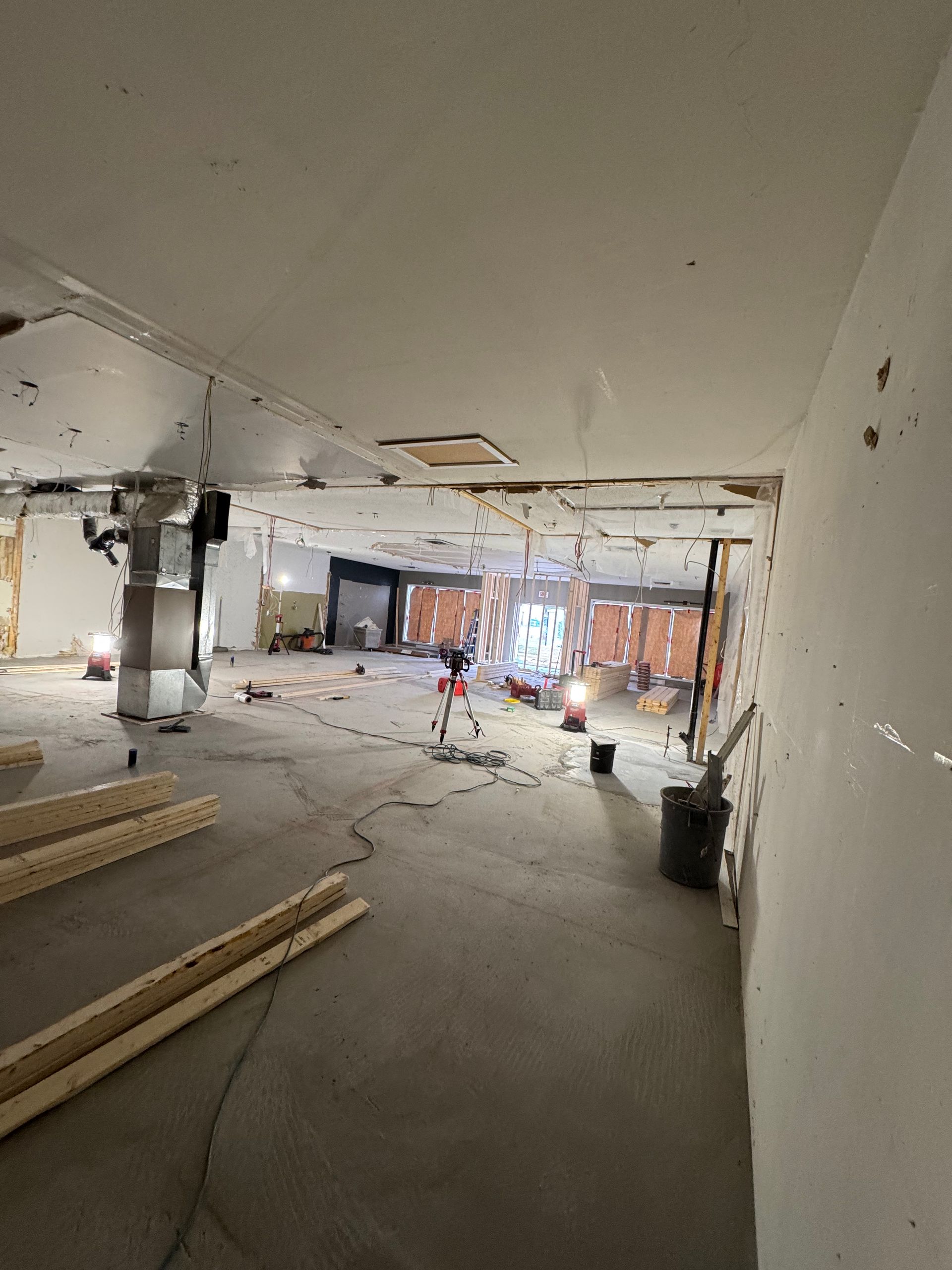 Intérieur spacieux et inachevé, avec plafond apparent, matériaux de construction éparpillés et lumière vive provenant du fond.