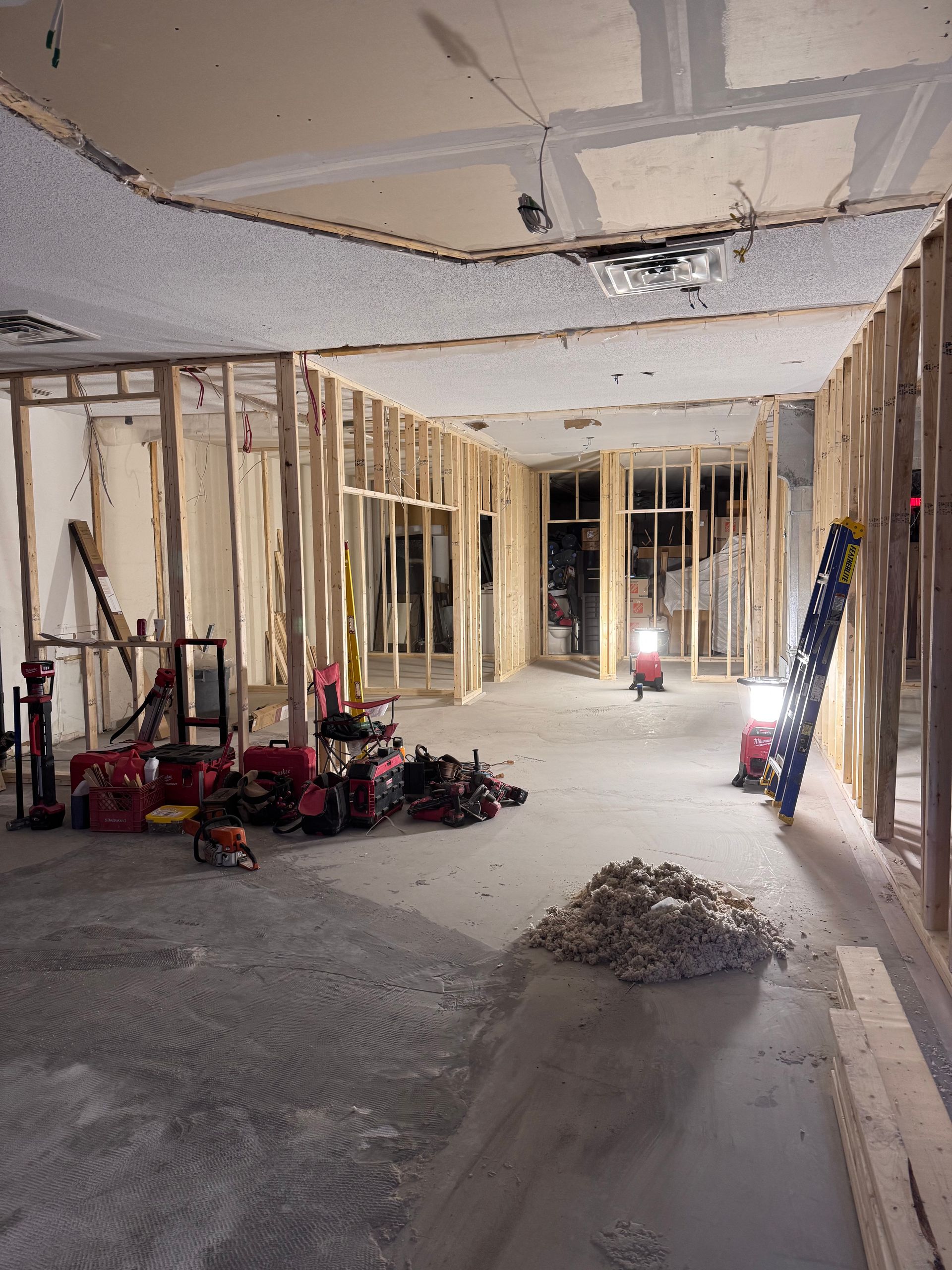 Intérieur en travaux avec charpente apparente, matériaux de plafond suspendus, outils et débris au sol.