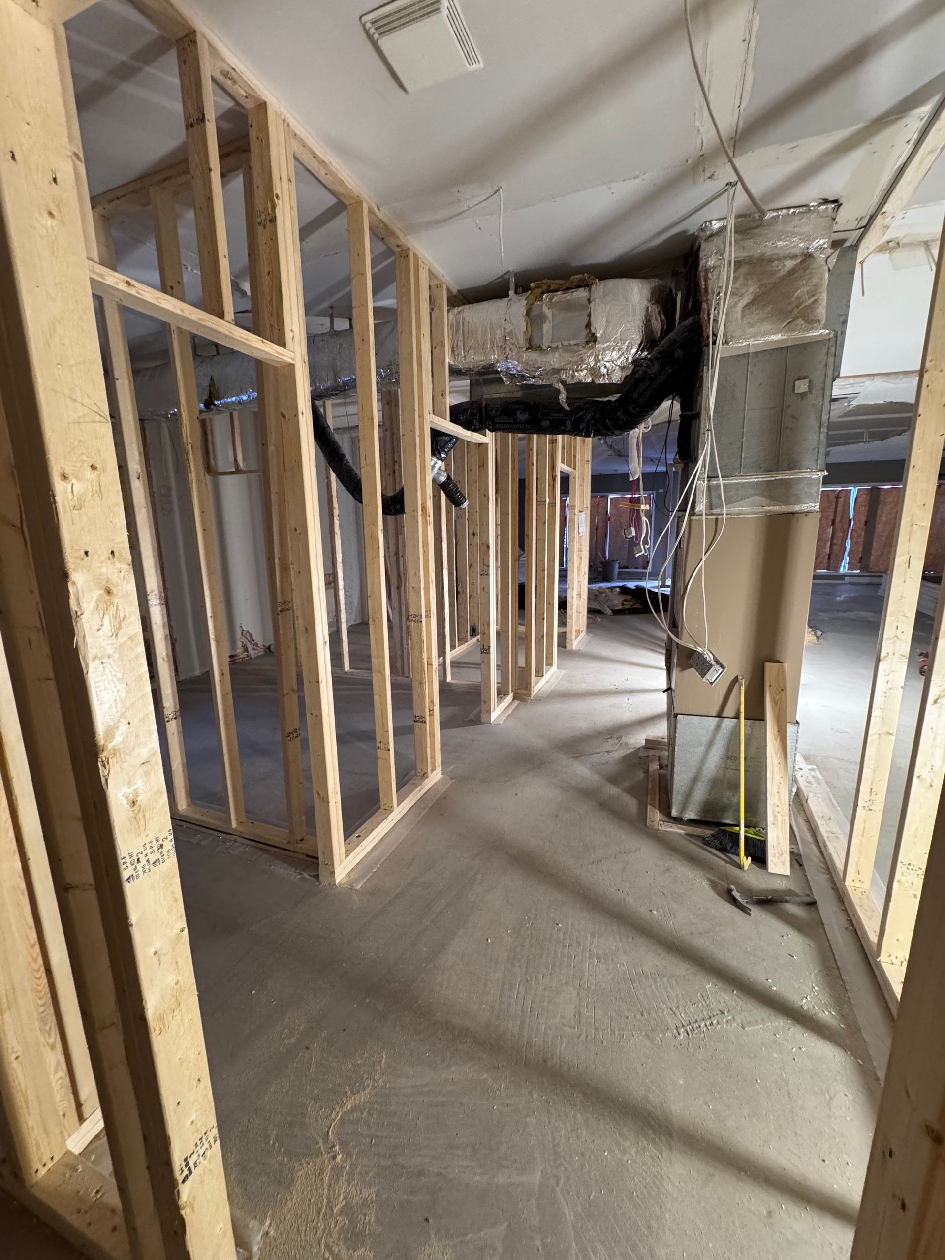 Couloir partiellement démoli avec montants muraux apparents, débris et conduits d'aération suspendus sur un chantier de rénovation