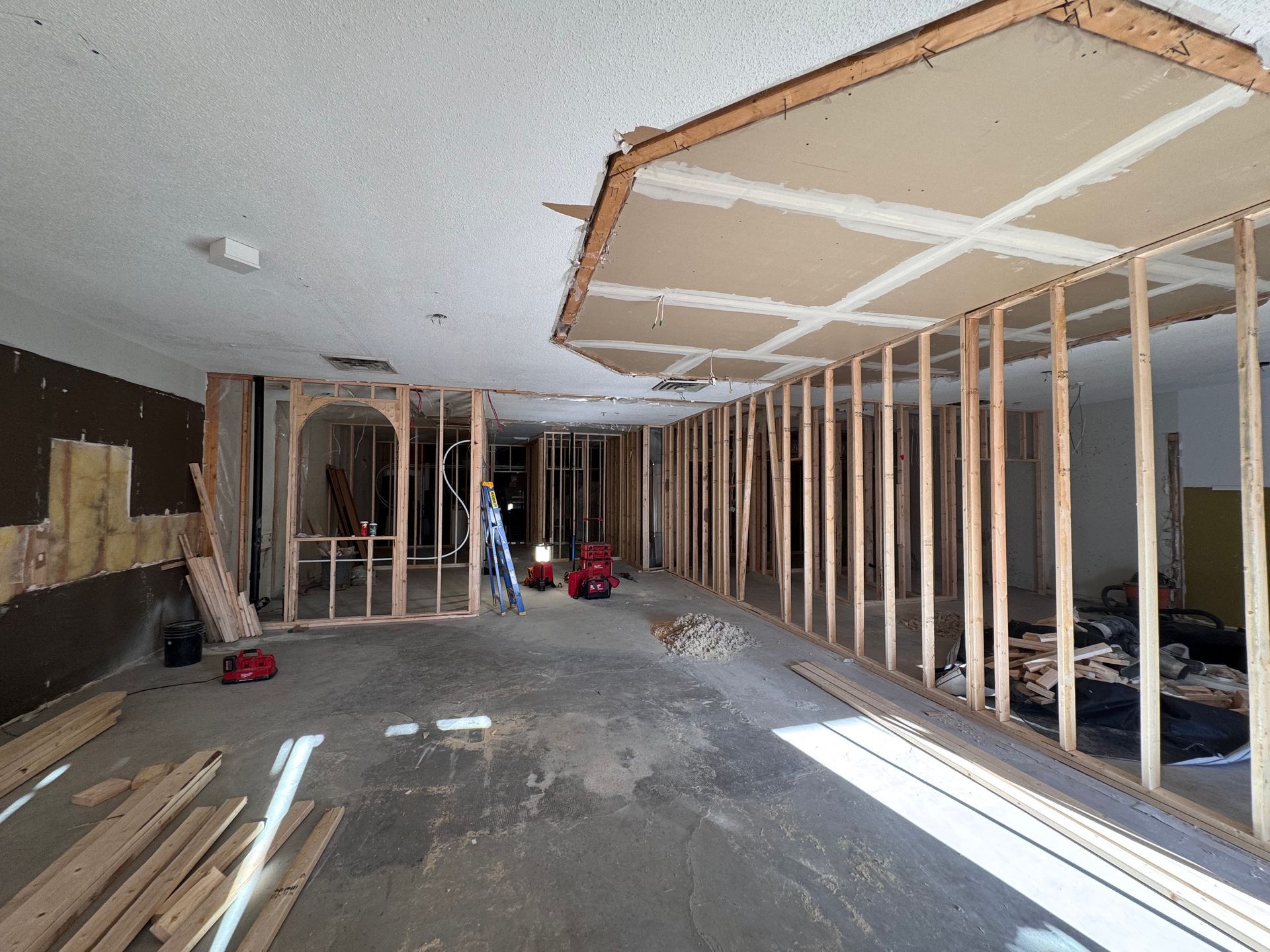Intérieur en rénovation avec charpente apparente, plafond inachevé et matériaux de construction éparpillés sur le sol.